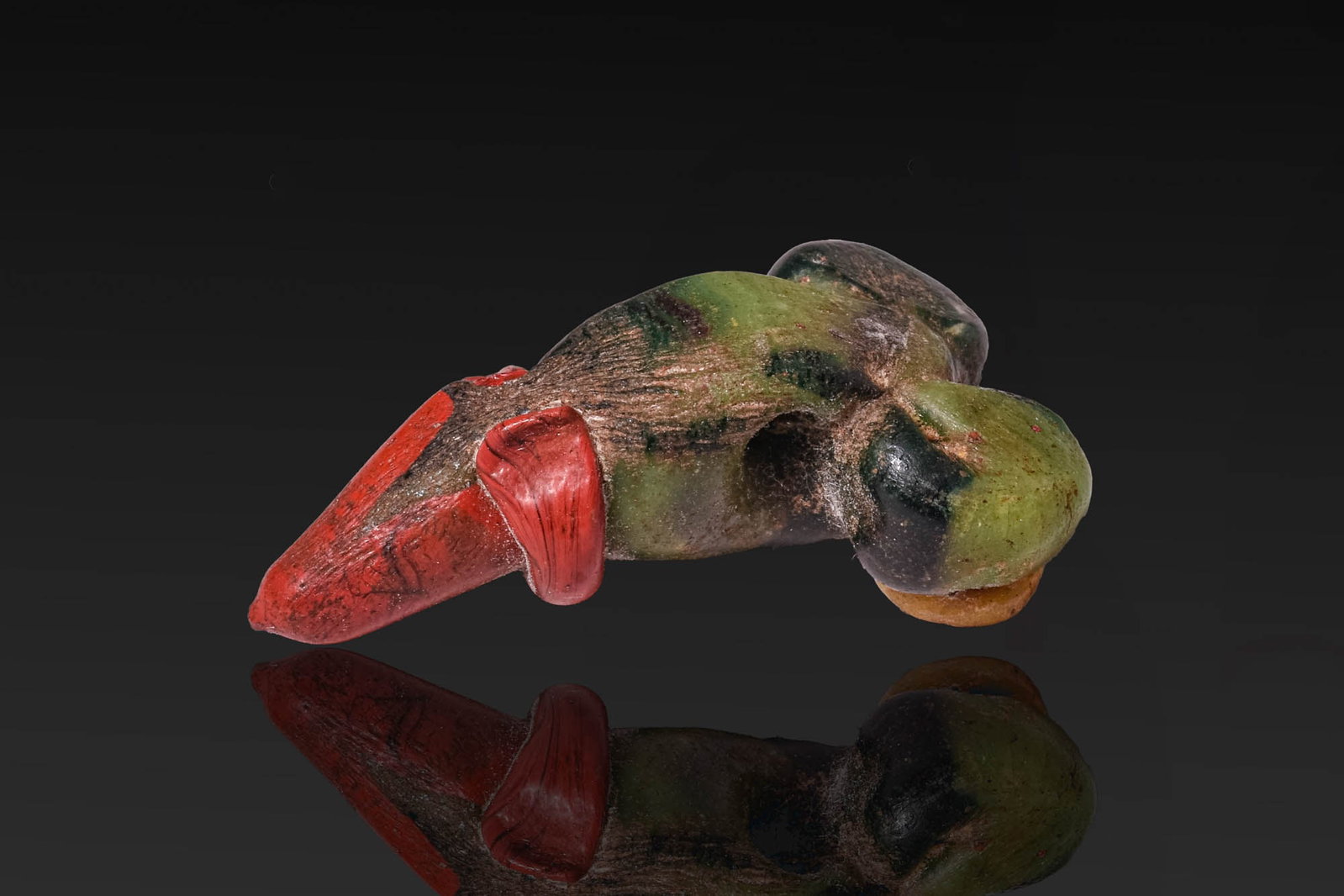 ROMAN GLASS PHALLIC AMULET: Ca. 200 BC - AD 100. A rod-formed glass phallic amulet in dark green with pale green streaks, pierced through the shaft for suspension. The tip is in red glass and rimmed by an applied red thread. Two