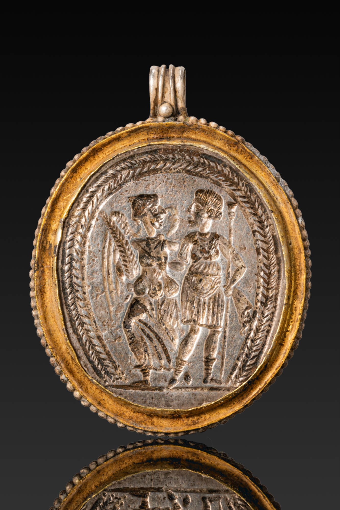 PHOENICIAN STYLE PHALLUS PENDANT: . A hollow glass phallus pendant with polychrome marvered trails to the shaft, red glans and testicles, a short foot in dark green with yellow horizontal bands, and a red suspension loop to the side. 