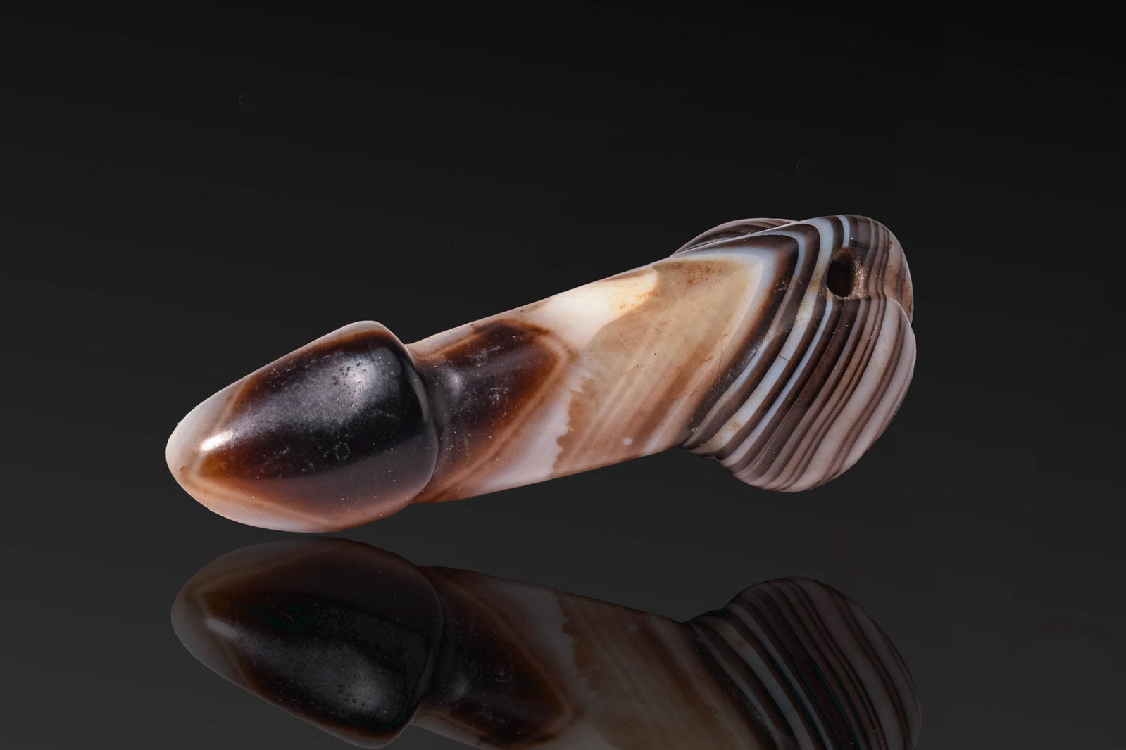 PHOENICIAN STYLE PHALLUS PENDANT: . An agate phallus pendant carved with a pointed glans, a tapering shaft drilled for suspension, and rounded testicles. Size: 70mm x 25mm; Weight: 40g Provenance: Private UK collection; From an old Br