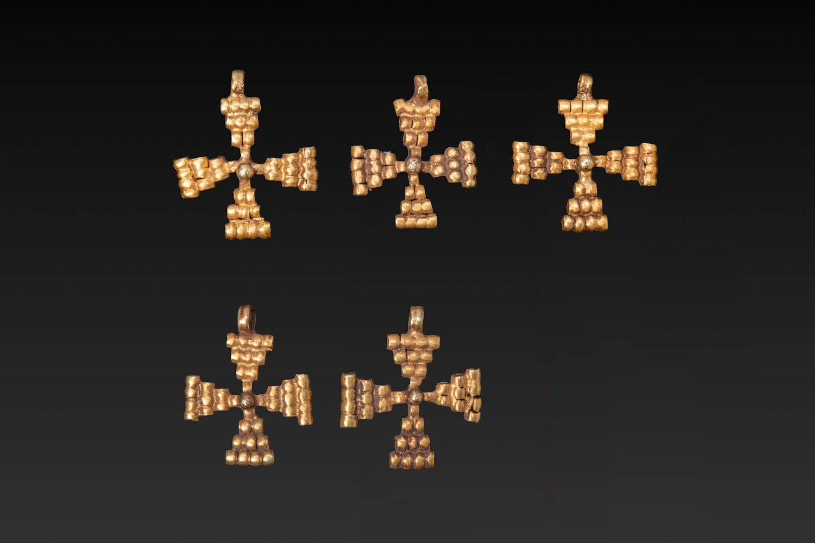 COLLECTION OF BYZANTINE GOLD CROSS PENDANTS: Ca. AD 500 - 600. A collection of five gold cross pendants, each with triangular arms built from clusters of short cylindrical elements arranged in graduated rows around a central granule. The upper a