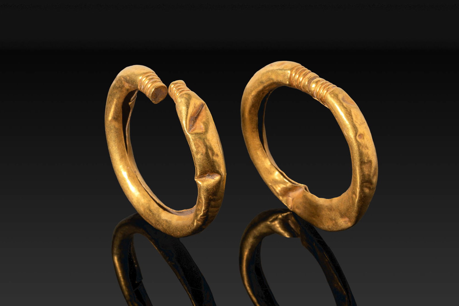 PAIR OF VIKING GOLD BRACELETS WITH RIBBED FINIALS: Ca. AD 700 - 900. A pair of hollow penannular bracelets, each made from thin sheet gold, with a thick rounded hoop tapering towards ribbed finials. Size: 51-51mm x 58-59mm; Weight: 31.1g Provenance: P