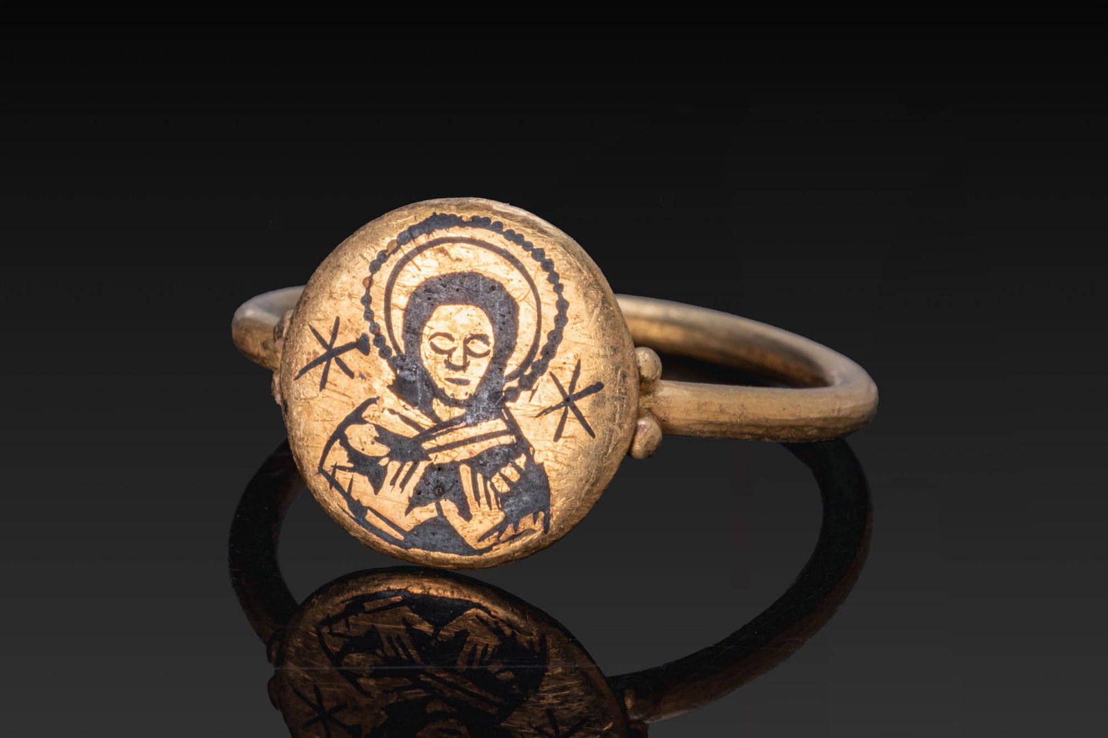 BYZANTINE GOLD AND NIELLO RING WITH BUST OF CHRIST: Ca. AD 500 - 700. A gold ring with a plain round-section hoop and a circular bezel, flanked at each side by a pair of granules. The bezel is engraved and inlaid with niello with a haloed bust of Chris