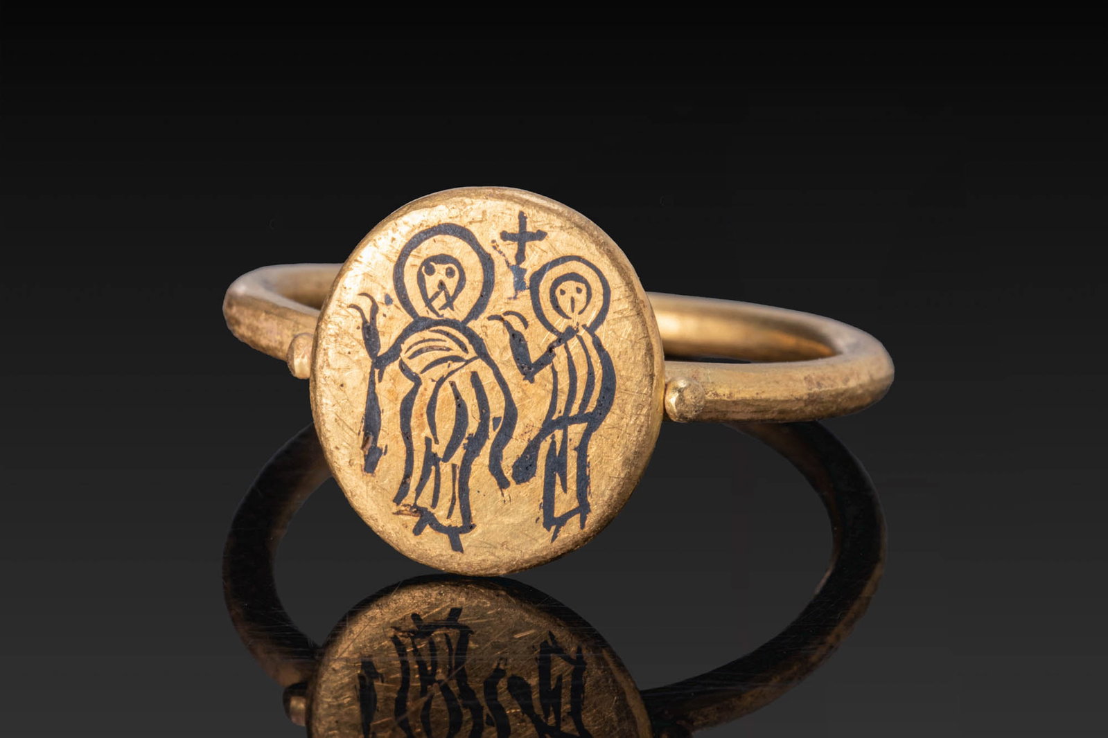 BYZANTINE GOLD AND NIELLO RING WITH DISCIPLES OF EMMAUS: Ca. AD 600. A gold ring with a slender hoop and a circular bezel inlaid with niello depicting two haloed standing figures beneath a cross, with gold pellets at either side of the bezel. Size: D:18.34m
