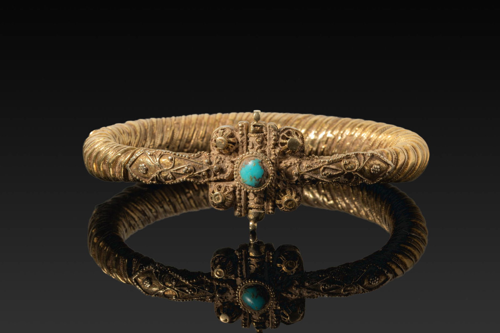 BYZANTINE GOLD ARMLET WITH CENTRAL TURQUOISE: Ca. AD 1000. An armlet made from sheet gold folded into a hollow tapering hoop with alternating ribs and ropework bands. The front section is decorated with scrollwork and filigree panels leading to a