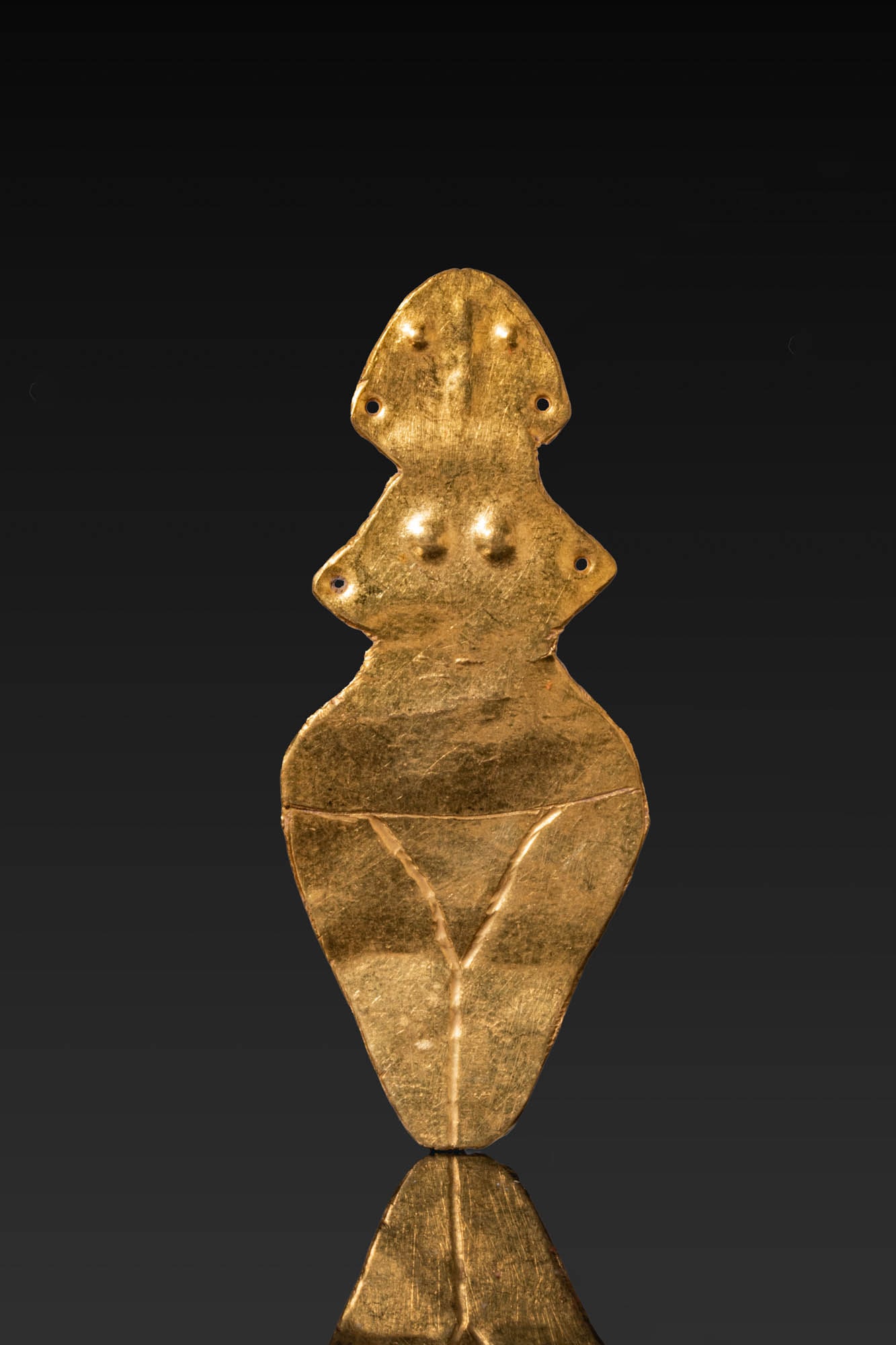 NEOLITHIC GOLD IDOL: Ca. 4600 - 4200 BC. A gold idol of stylised female form, cut from a thin sheet with a rounded head, projecting pierced ears and shoulders, repousse eyes and breasts, and a tapering lower body with an 