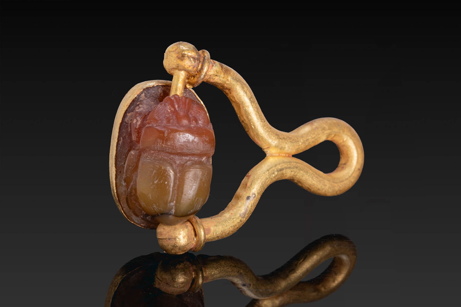 EGYPTIAN CARNELIAN SCARAB IN GOLD PENDANT: Late to Ptolemaic Period, Ca. 664 - 332 BC. A carnelian scarab with a carved head, divided wing cases, and a plain underside. Mounted in a gold pendant with an oval cell, a round-section shank, and a 