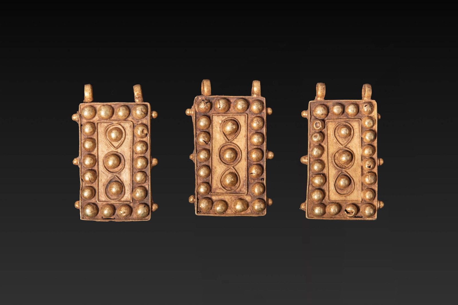 COLLECTION OF HEAVY GREEK GOLD BELT APPLIQUES: Ca. 300 - 100 BC. A collection of three rectangular gold belt appliques, each decorated on the obverse with repousse bosses arranged in a central panel and in an outer border, framed by twisted wire. 