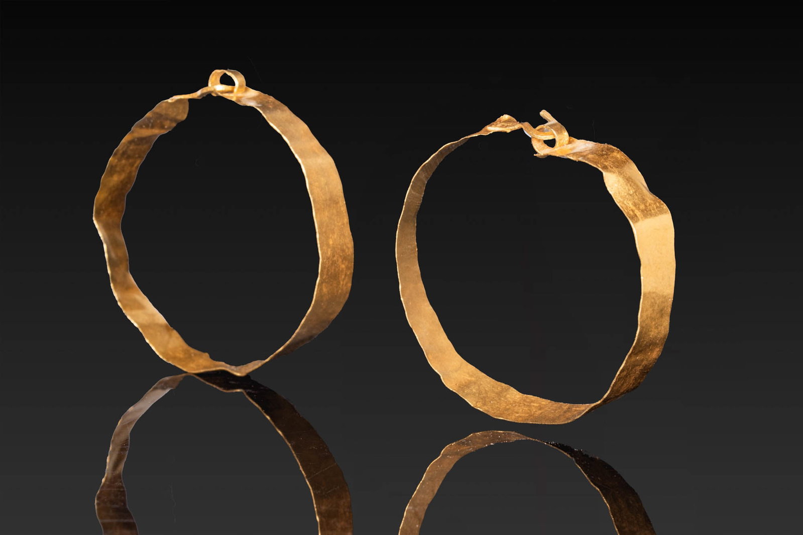 MATCHED PAIR OF GREEK GOLD EARRINGS: Ca. 500 - 300 BC. A matched pair of gold earrings, each formed as a broad hoop of flattened sheet gold with one end tapering to a hooked terminal that passes through a small loop at the other. Size: 3