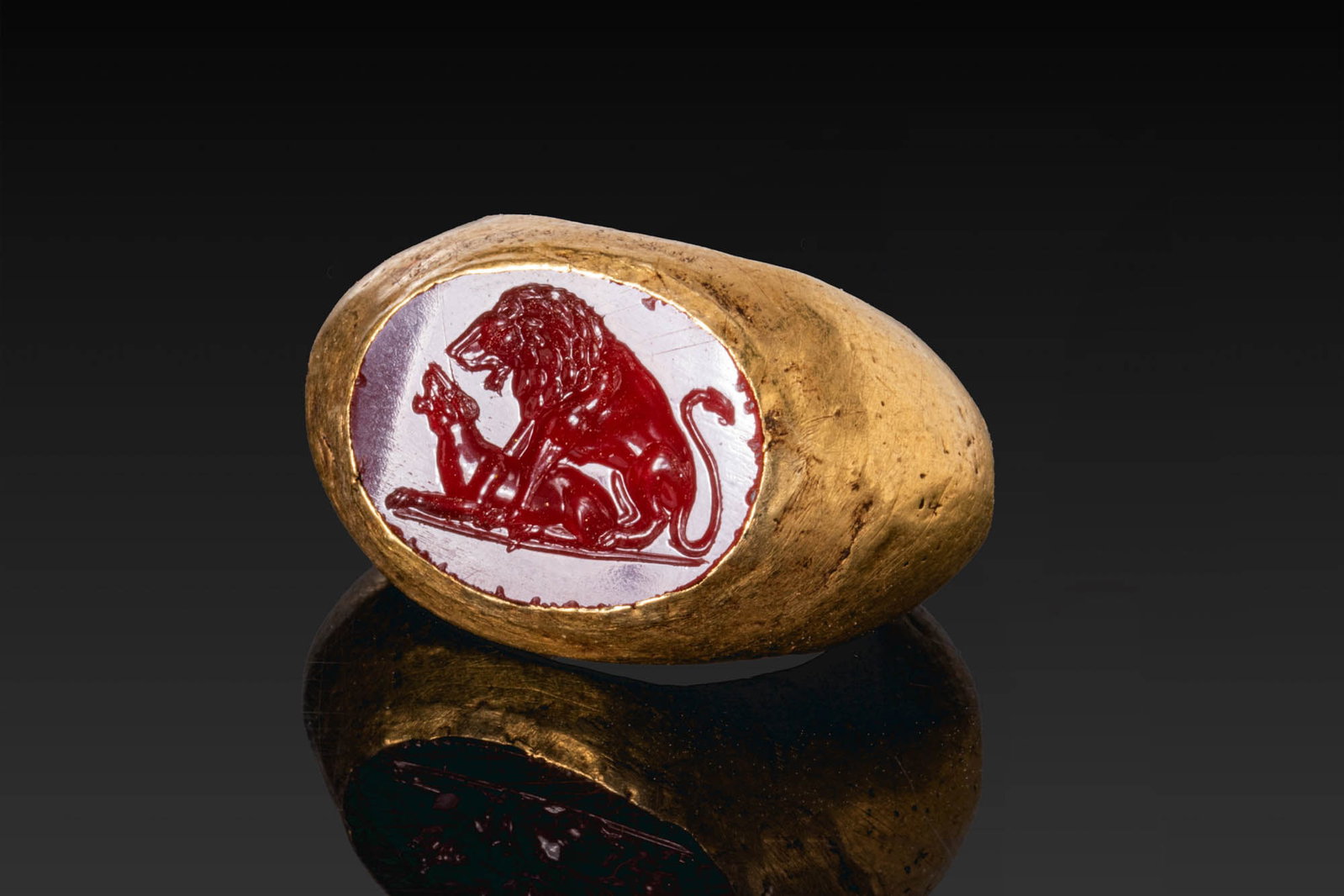 HELLENISTIC CARNELIAN INTAGLIO OF A LION AND LIONESS IN GOLD RING: Ca. 200 - 100 BC. A carnelian intaglio engraved with a lion seated to the right above a lioness reclining to the left on a groundline, his forepaws extended over her back. It is set in a possibly late