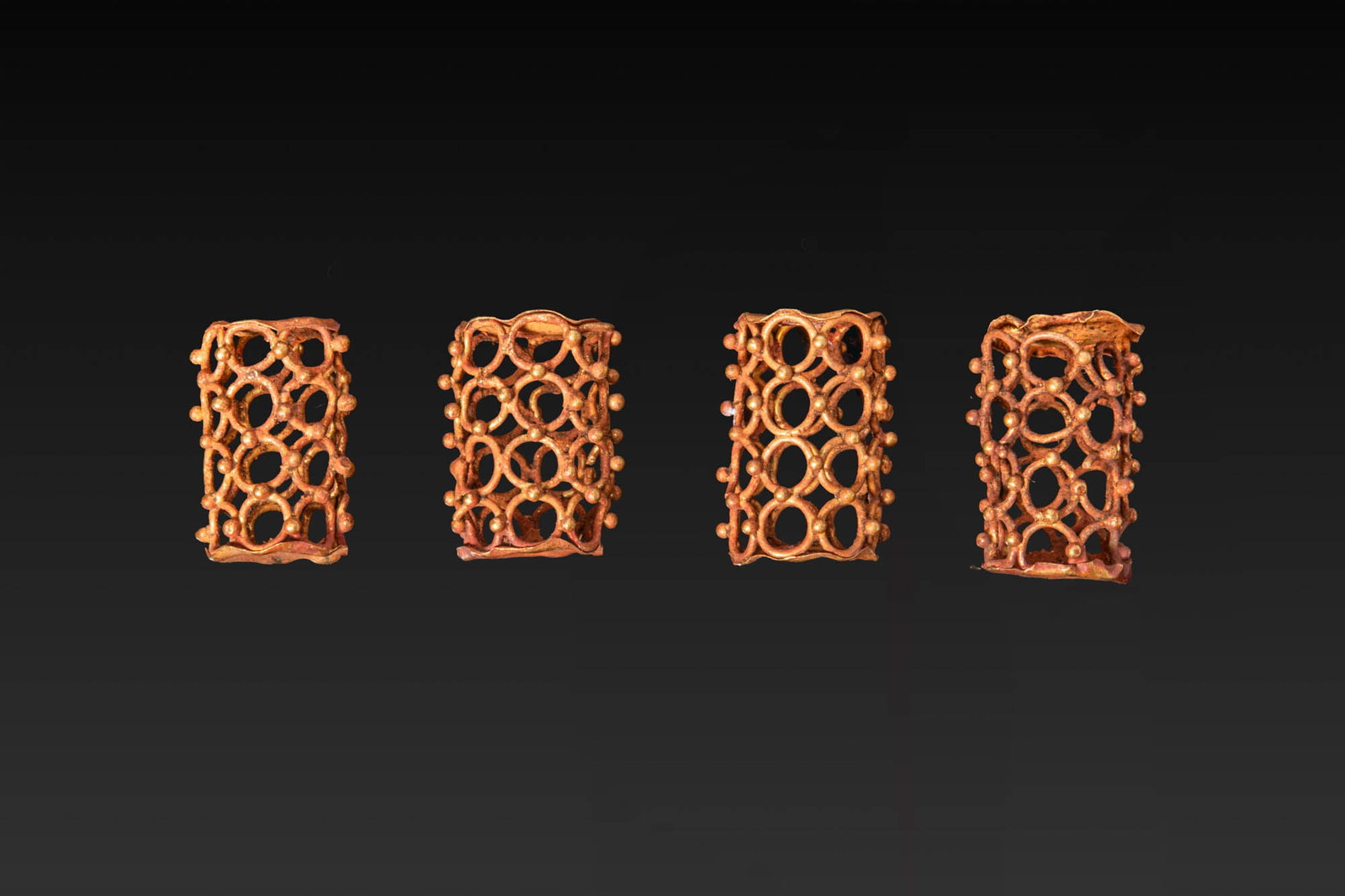 COLLECTION OF GREEK GOLD CAGE BEADS: Ca. 800 - 600 BC. A collection of four gold cage beads, each with an openwork cylindrical body composed of linked circular loops joined by granules, and with perforated plain circular ends. Size: 13-1