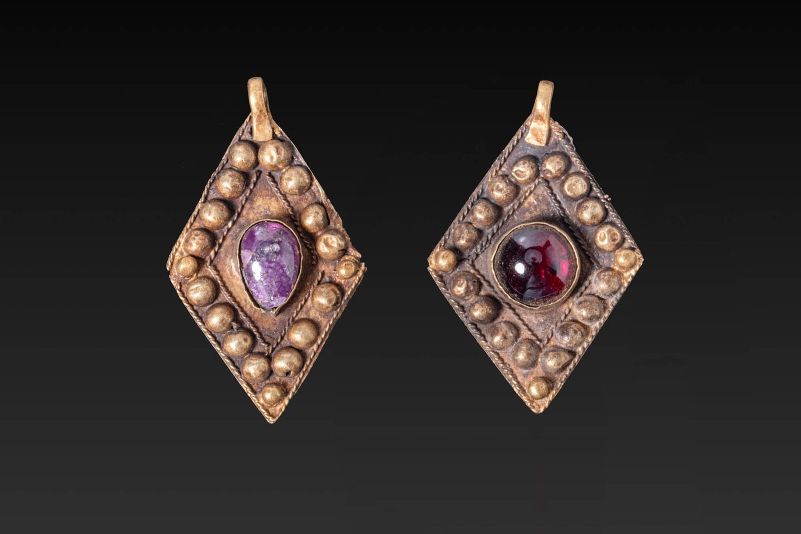 PAIR OF HELLENISTIC GOLD PENDANTS WITH CENTRAL CABOCHONS: Ca. 300 - 100 BC. A pair of gold pendants, each lozenge-shaped and centred with a cabochon set within a plain mount, framed by twisted wire and an outer border of bosses, with a suspension loop above.