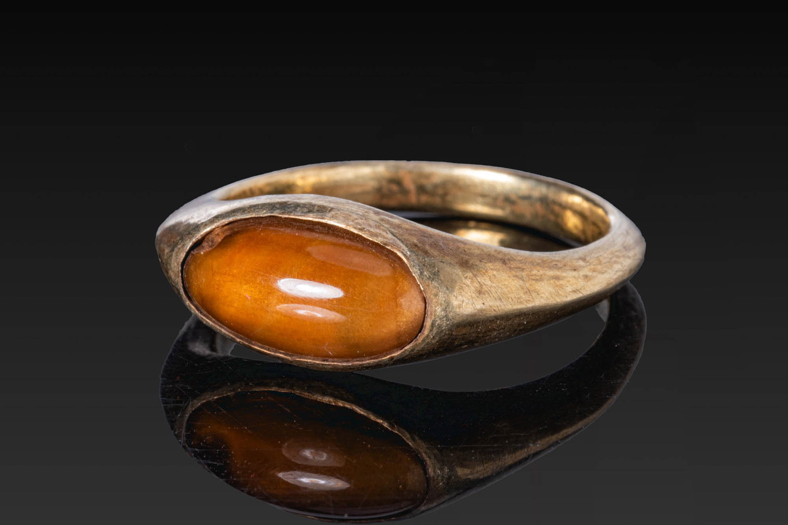 HELLENISTIC GOLD RING WITH ORANGE STONE CABOCHON: Ca. 100 BC. A gold ring with a flattened hoop and an elongated oval setting containing an orange stone cabochon. For similar see: The British Museum, Museum number 1917,0501.387. Size: D:18.14mm / US: