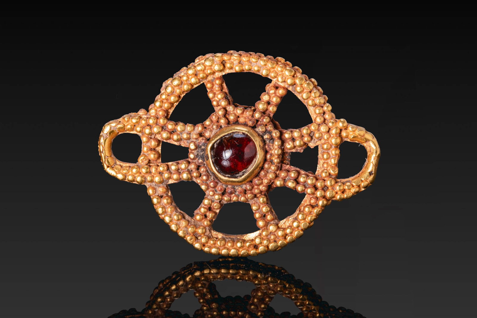 HELLENISTIC GOLD GRANULATED PENDANT WITH RED GARNET CABOCHON: Ca. 300 - 100 BC. A gold pendant of openwork roundel form, granulated throughout and set at the centre with a red garnet cabochon in a circular cell. Size: 28mm x 21mm; Weight: 7.7g Provenance: Privat