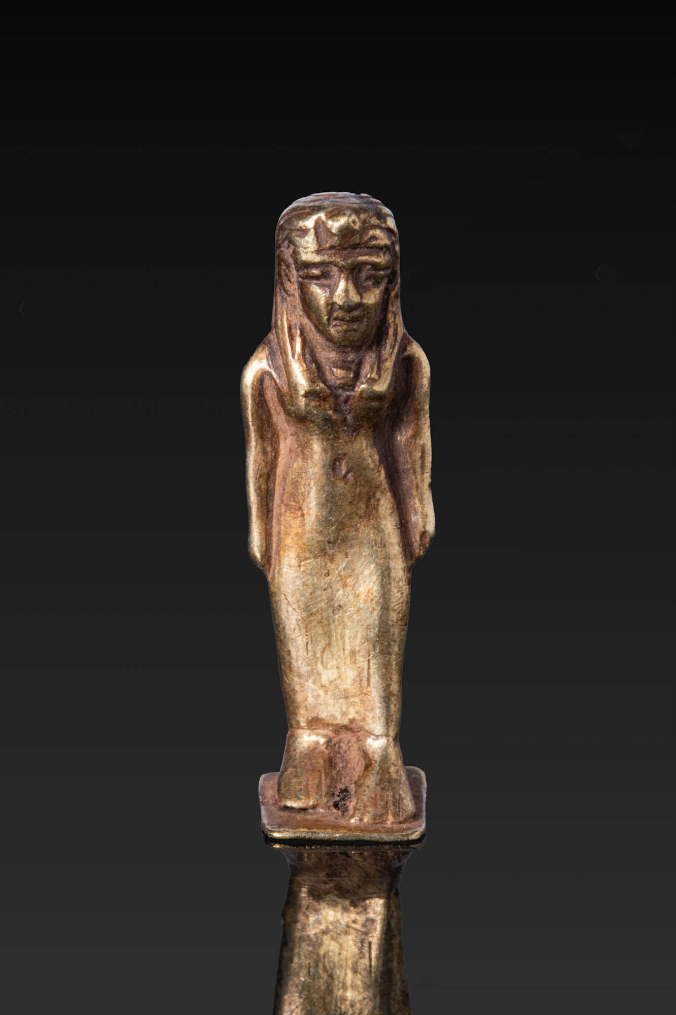 PHOENICIAN GOLD PENDANT OF ISIS: Ca. 600 - 400 BC. A gold pendant of Isis standing on an integral flat base, wearing a tripartite wig and a long close-fitting sheath dress revealing the navel, with her arms held close to her sides an