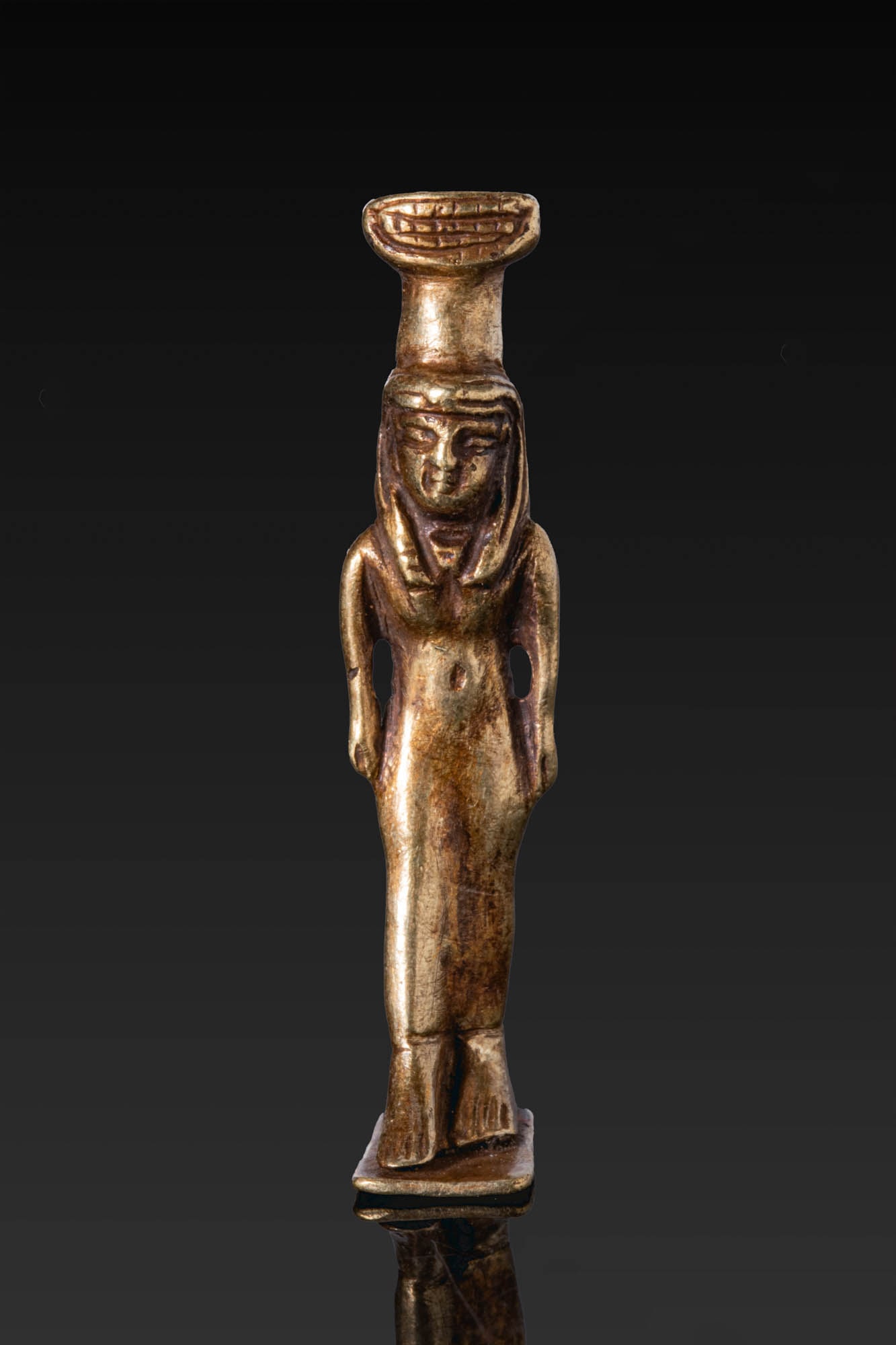 PHOENICIAN GOLD PENDANT OF NEPHTHYS: Ca. 600 - 400 BC. A gold pendant of Nephthys standing with her right leg advancing on an integral flat base, wearing a tripartite wig and a long, close-fitting sheath dress revealing the navel, with h
