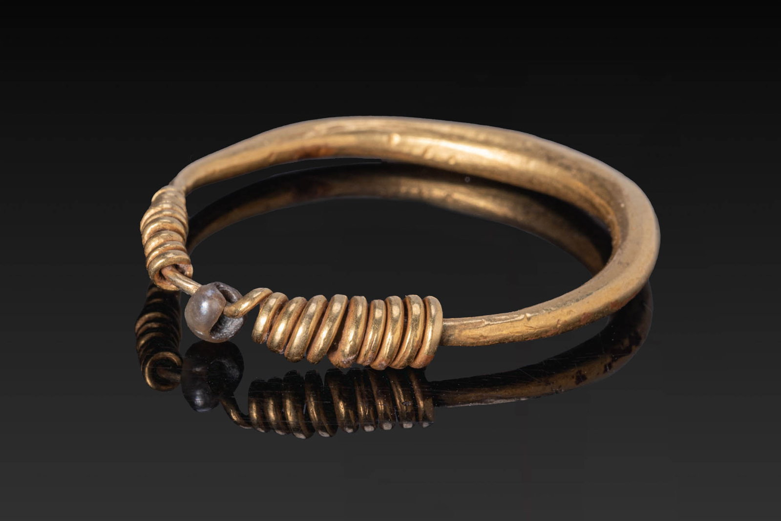 PHOENICIAN GOLD RING WITH PEARL: Ca. 500 BC. A gold ring formed as a tapering hoop with overlapping coiled terminals, with a pearl bead between them. For similar see: The British Museum, Museum Number 133455. Size: 31mm x 28mm; Weigh