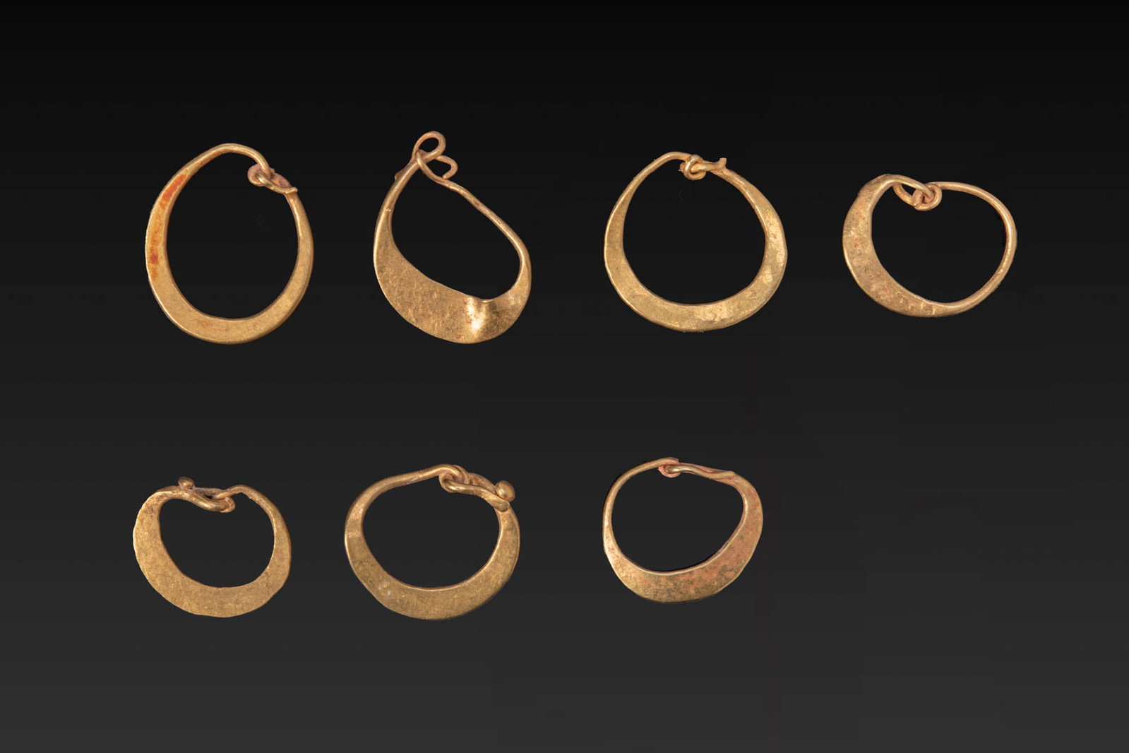 COLLECTION OF ROMAN GOLD EARRINGS: Ca. AD 1 - 300. A collection of seven gold earrings, each a flat hoop of tapering profile with overlapping terminals. Size: 12-14mm x 10-11mm; Weight: 4g Provenance: From a London private collection; 