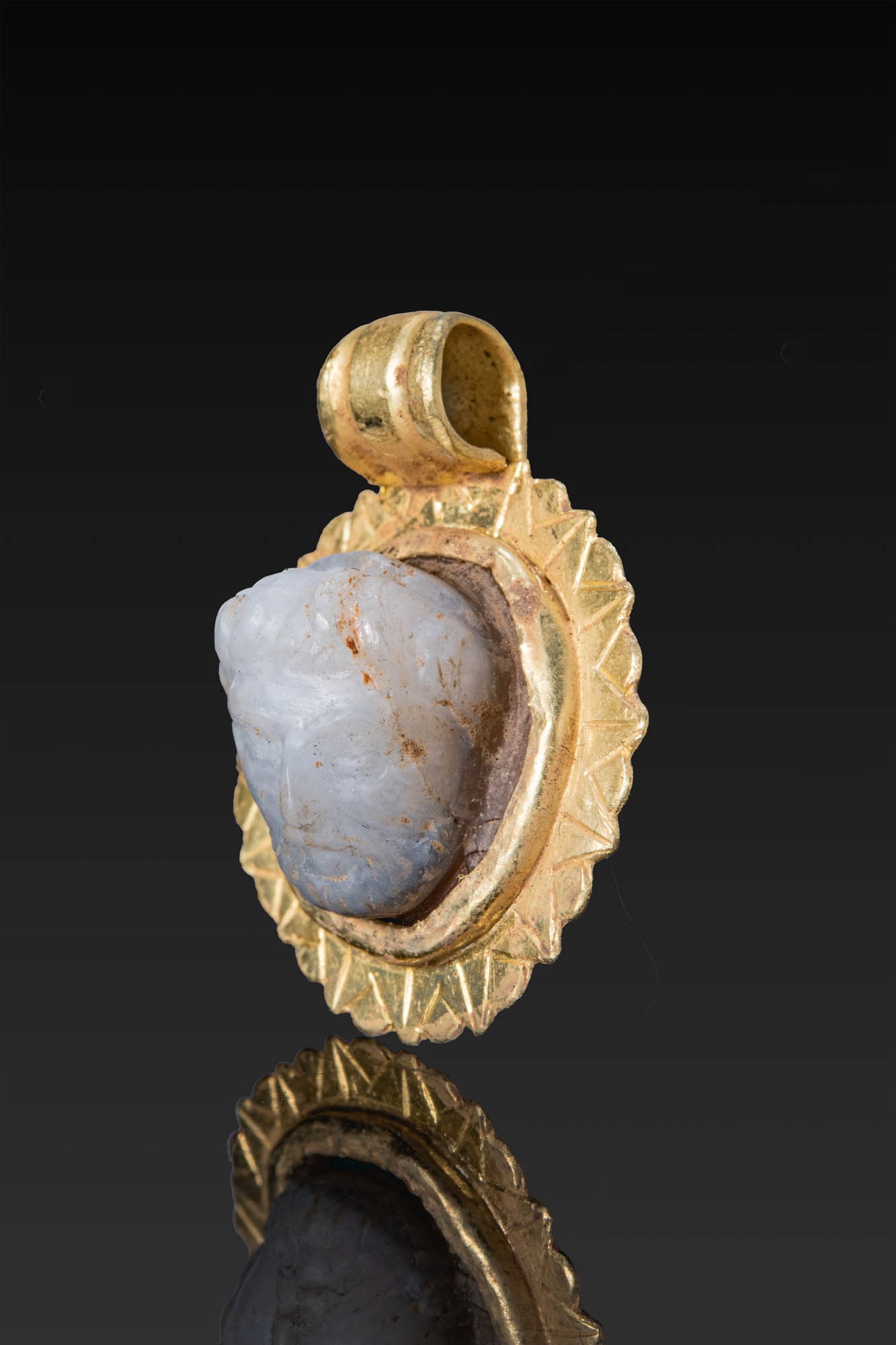 ROMAN AGATE CAMEO OF MAN IN GOLD PENDANT: Ca. AD 1 - 300. An agate cameo carved with a head, turned slightly to the left, with curly hair, a beard, and a prominent nose. The stone is set in a circular gold pendant with a plain collar and a sc