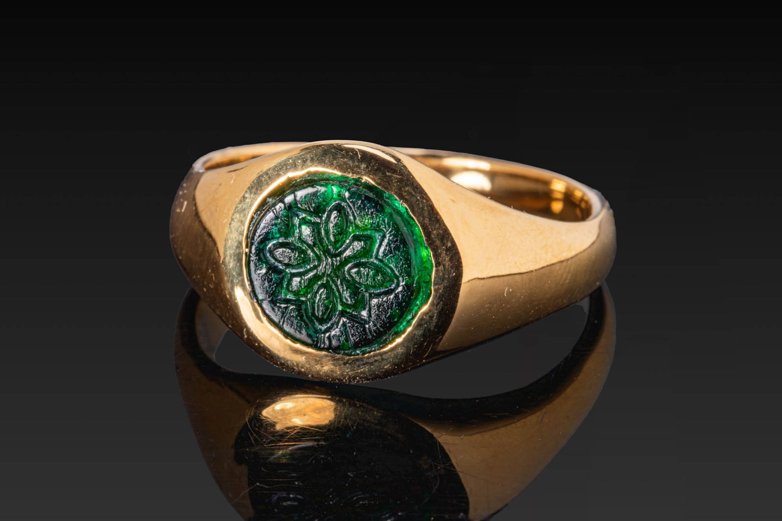 LATE ROMAN GREEN GLASS GEM WITH STAR IN GOLD RING: Ca. AD 100 - 300. A green glass gem engraved with a star, mounted in a possibly later gold ring with a broad tapering hoop and a circular bezel. Size: D:18.14mm / US: 8 / UK: P 1/2; Weight: 8g Provena