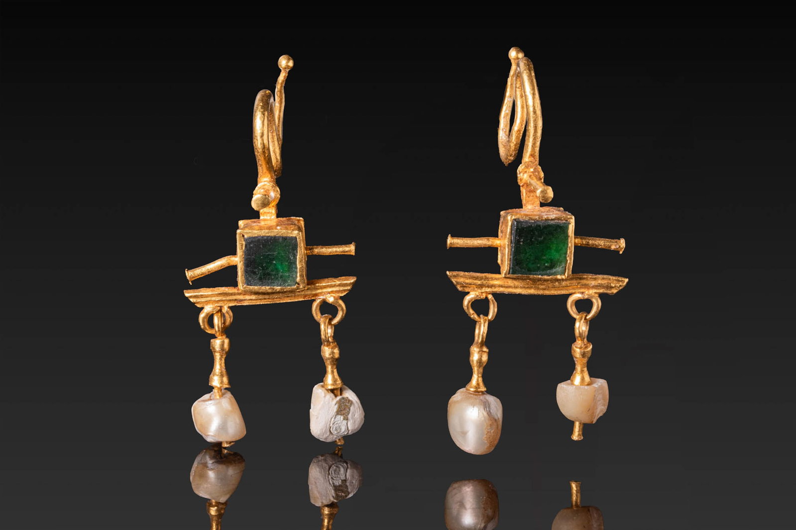 MATCHED PAIR OF ROMAN OR BYZANTINE GOLD EARRINGS WITH GREEN GLASS AND PEARL DROPS: Ca. AD 200 - 400. A matched pair of gold earrings, each with an S-shaped ear wire and centred on a square green glass gem in a box setting, flanked by short lateral projections and set above a horizon