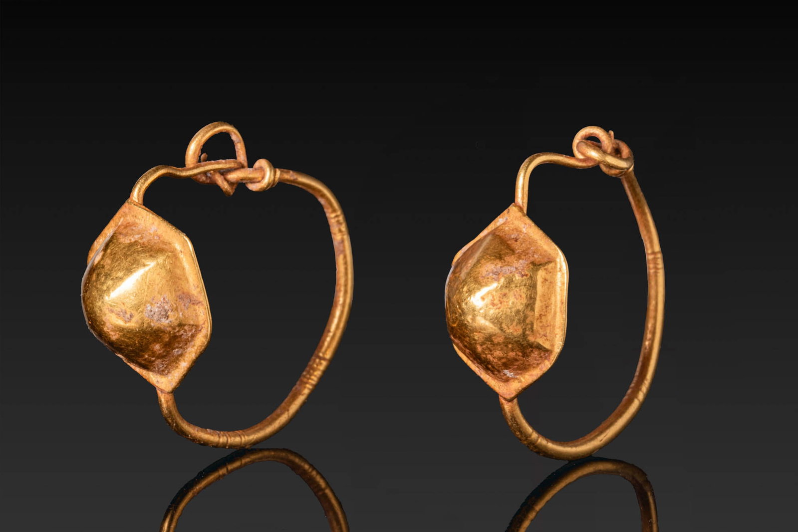 MATCHED PAIR OF ROMAN GOLD EARRINGS: Ca. AD 1 - 300. A matched pair of gold earrings, each with a round-section tapering hoop centred on a sheet-gold element with a hexagonal base and a faceted domed body. Size: 22-23mm x 21-22mm; Weight