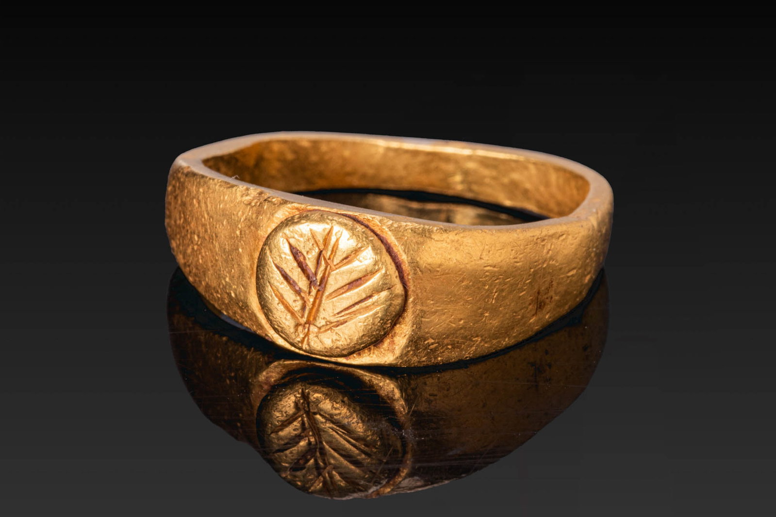 LATE ROMAN GOLD RING WITH PALM BRANCH: Ca. AD 100 - 300. A gold ring with a tapering hoop and a raised circular bezel engraved with a palm branch. For similar see: The British Museum, Museum number 1917,0501.163. Size: D:15.7mm / US: 5 / U