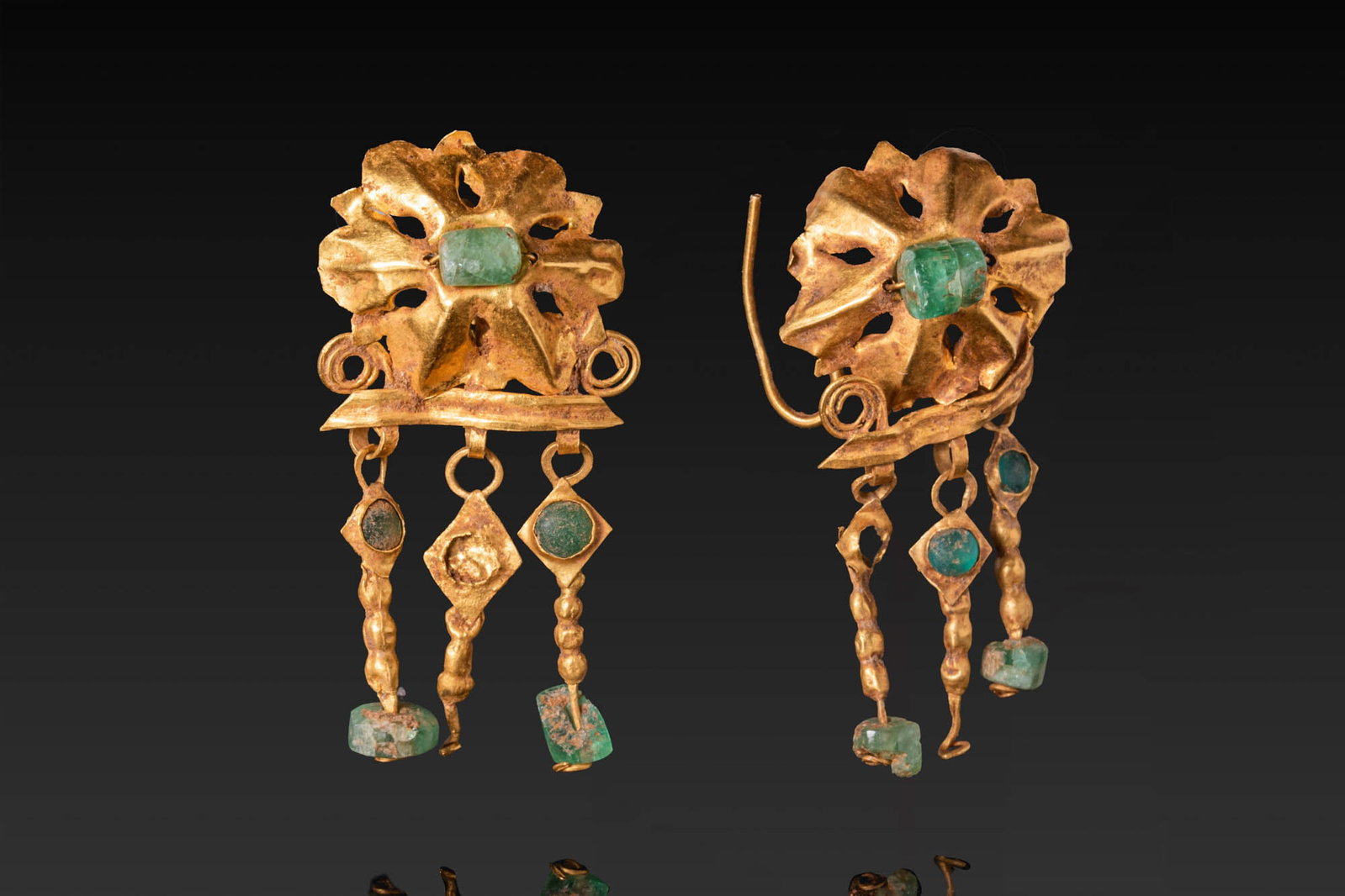 MATCHED PAIR OF ROMAN GOLD EARRINGS: Ca. AD 200 - 300. A matched pair of gold earrings, each with an ear wire at the rear and a rosette-shaped plaque centred on an emerald. Below is a horizontal bar with spiral terminals, from which hang