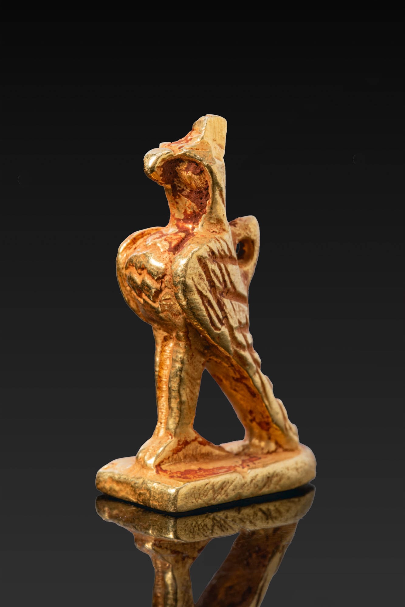 ROMAN LEGIONARY EAGLE PENDANT: Ca. AD 1 - 200. A gold pendant in the form of an eagle standing upright on a flat base, with the head held high, a hooked beak, and a small crest. The folded wings are incised with plumage, and a susp