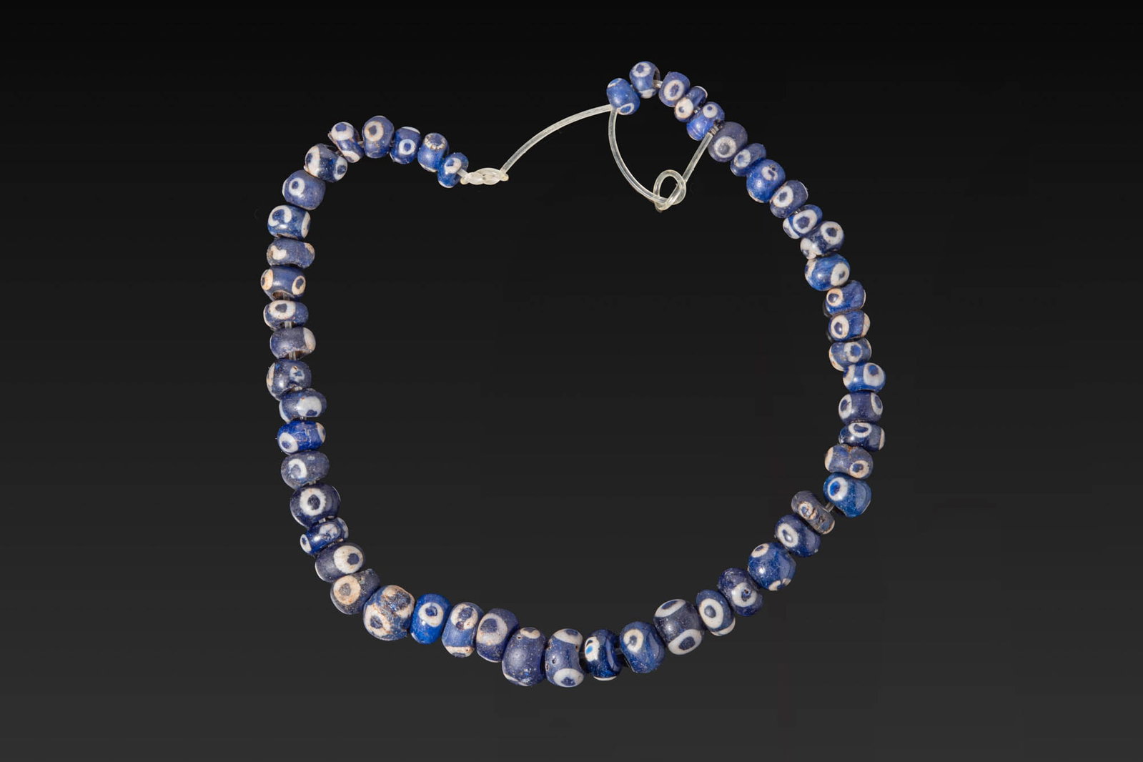 LARGE NECKLACE OF PHOENICIAN GLASS EYE BEADS: Ca. 600 - 300 BC. A strand of 54 deep blue glass beads of annular shape, each decorated with white and blue eye motifs. For similar see: The Metropolitan Museum of Art, Object Number: 74.51.13. Size: 