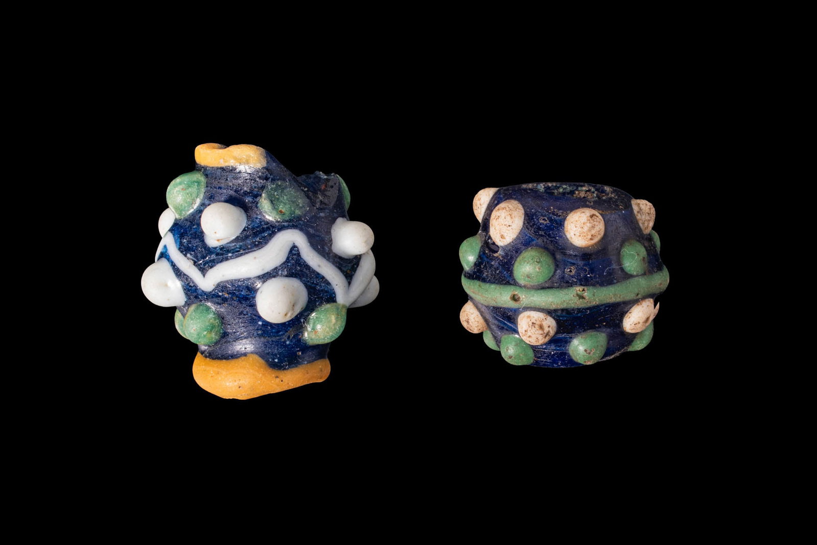 PAIR OF PHOENICIAN POLYCHROME LARGE BEADS: Ca. 400 - 200 BC. A pair of glass beads, each of compressed globular form with a central perforation and a dark blue ground. The bead on the left is decorated with yellow collars, a central white zigz