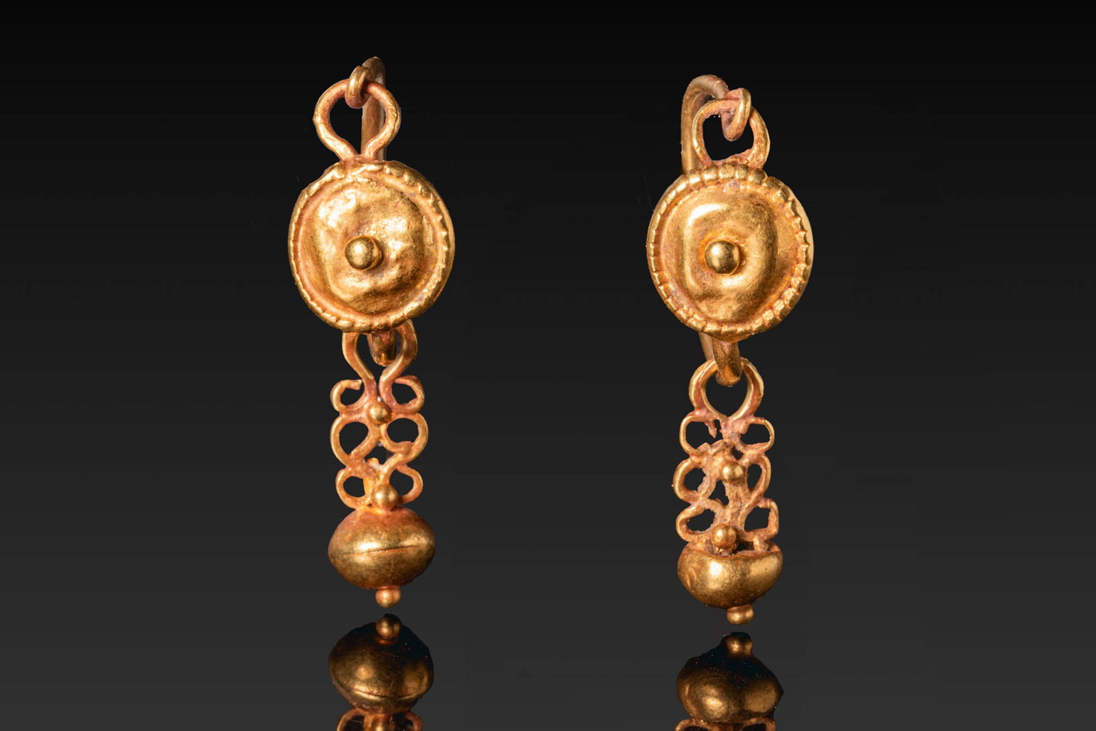 MATCHED PAIR OF ROMAN GOLD EARRINGS WITH OPENWORK DROPS: Ca. AD 1 - 300. A matched pair of gold earrings, each with a tapering, round-section hoop centred on a slightly domed circular plaque with a raised boss and a notched border, suspending an openwork dr