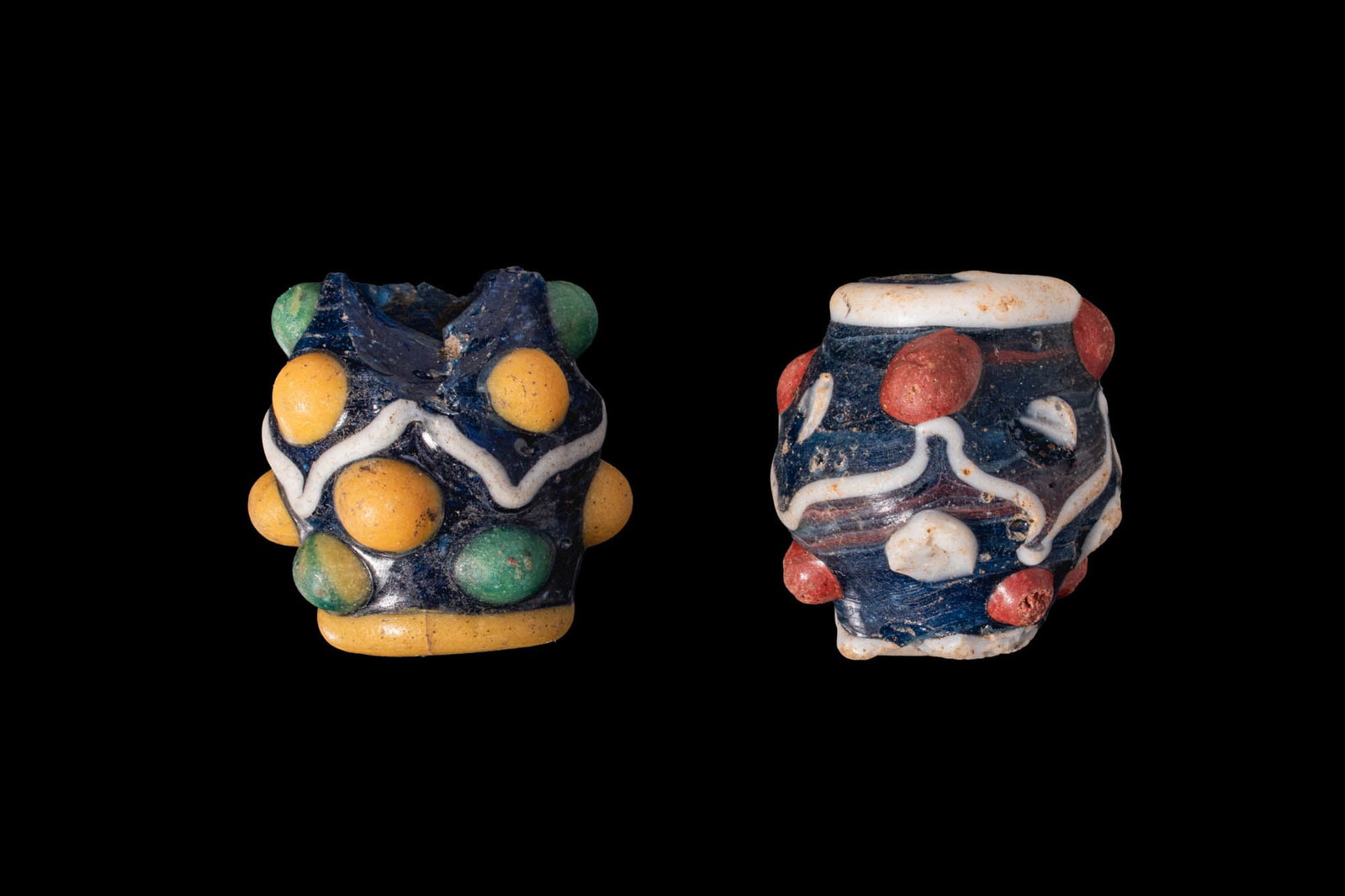 PAIR OF PHOENICIAN POLYCHROME LARGE BEADS: Ca. 400 - 200 BC. A pair of glass beads, each of compressed globular form with a central perforation and a dark blue ground. The bead on the left is decorated with a yellow collar, a central white zig