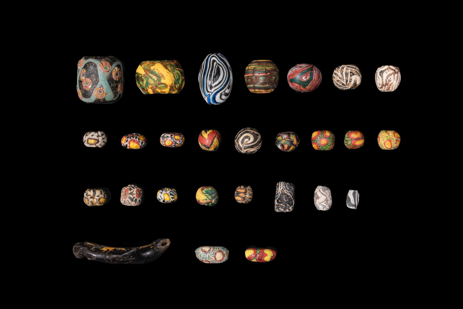 LARGE COLLECTION OF ROMAN MOSAIC GLASS BEADS: Ca. 100 BC - AD 200. A collection of 27 opaque and translucent glass beads, including spherical and cylindrical examples, decorated with vivid polychrome canes, concentric eye motifs, and marbled and 