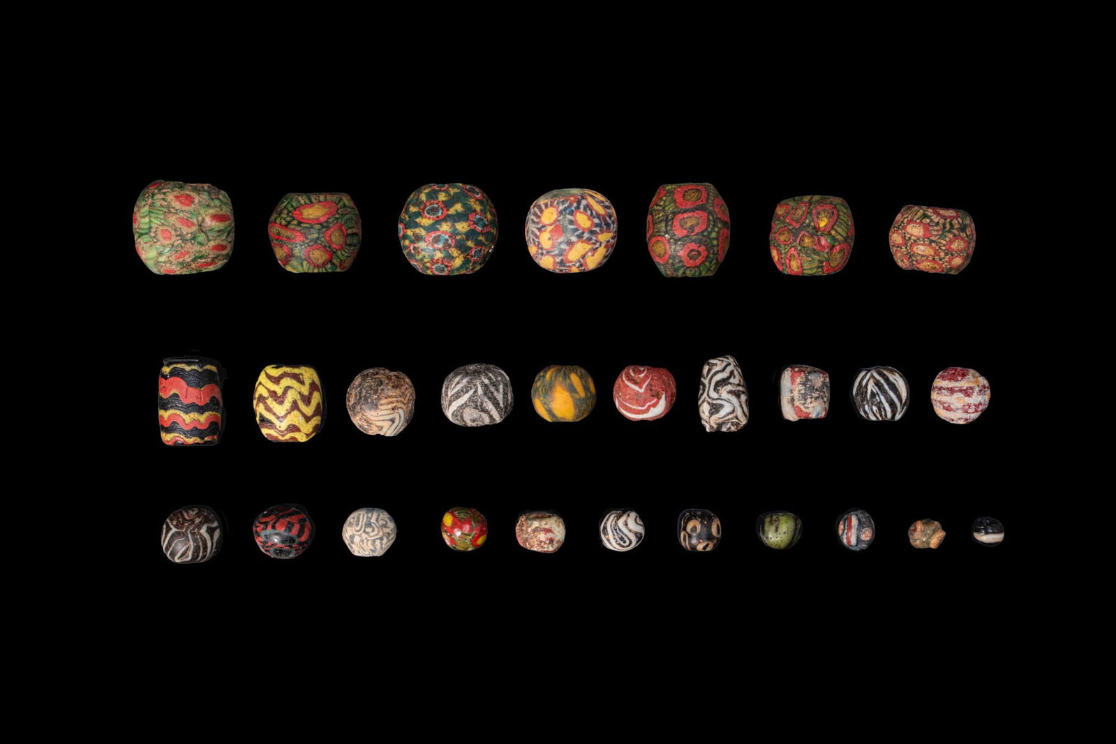 LARGE COLLECTION OF ROMAN MOSAIC GLASS BEADS: Ca. 300 BC - AD 200. A collection of 28 opaque and translucent glass beads, including spherical, biconical and cylindrical examples, decorated with vivid polychrome canes, concentric eye motifs, marbl