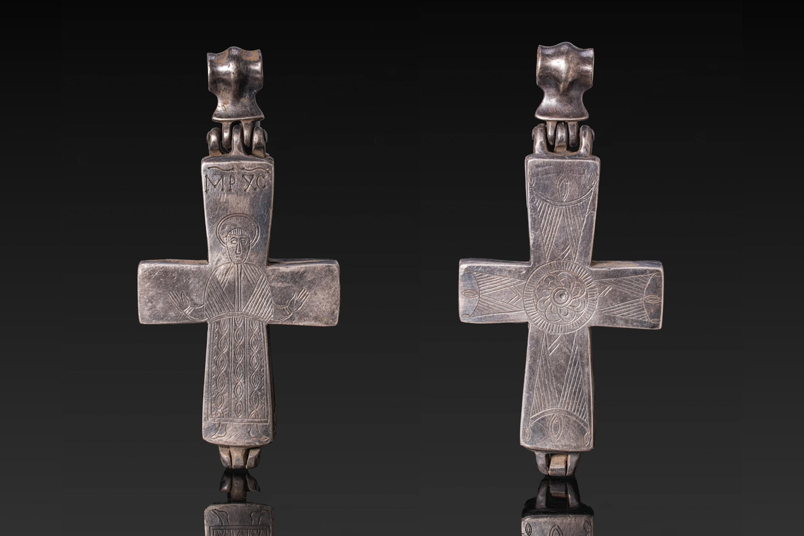 BYZANTINE SILVER ENKOLPION: Ca. AD 900 - 1100. A silver enkolpion cross pendant with a large suspension loop above a hinged fitting. The obverse is engraved with a haloed standing figure with arms outstretched, wearing a long