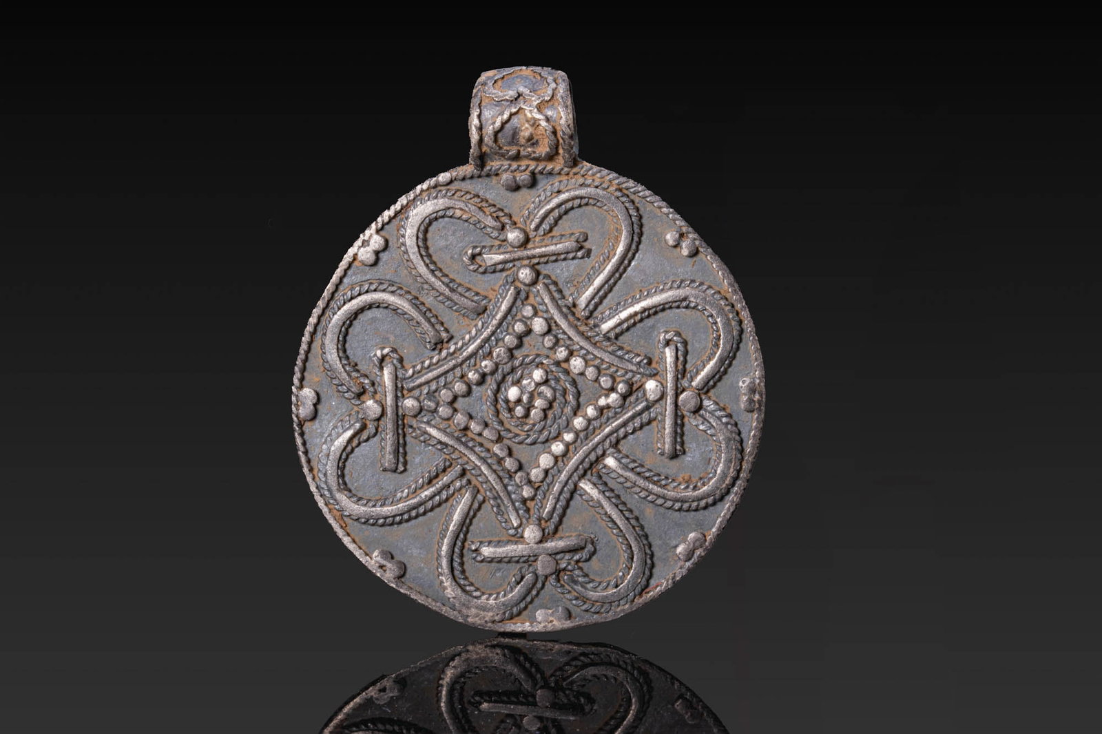 VIKING SILVER ROPEWORK MEDALLION: Ca. AD 700 - 900. A silver medallion with the obverse decorated with ropework arranged around a central granulated lozenge, with further pellets along the outer twisted wire border and a rolled