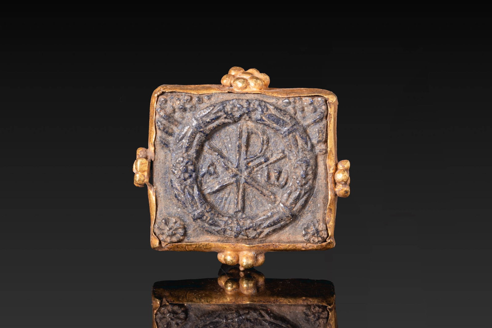 BYZANTINE GOLD AND LAPIS LAZULI PENDANT WITH CHI-RHO IN LAUREL CROWN: Ca. AD 700 - 900. A gold pendant of rectangular form, set with a lapis lazuli plaque carved with a Chi-Rho Christogram enclosed within a laurel wreath, with alpha and omega in the field. The frame is 