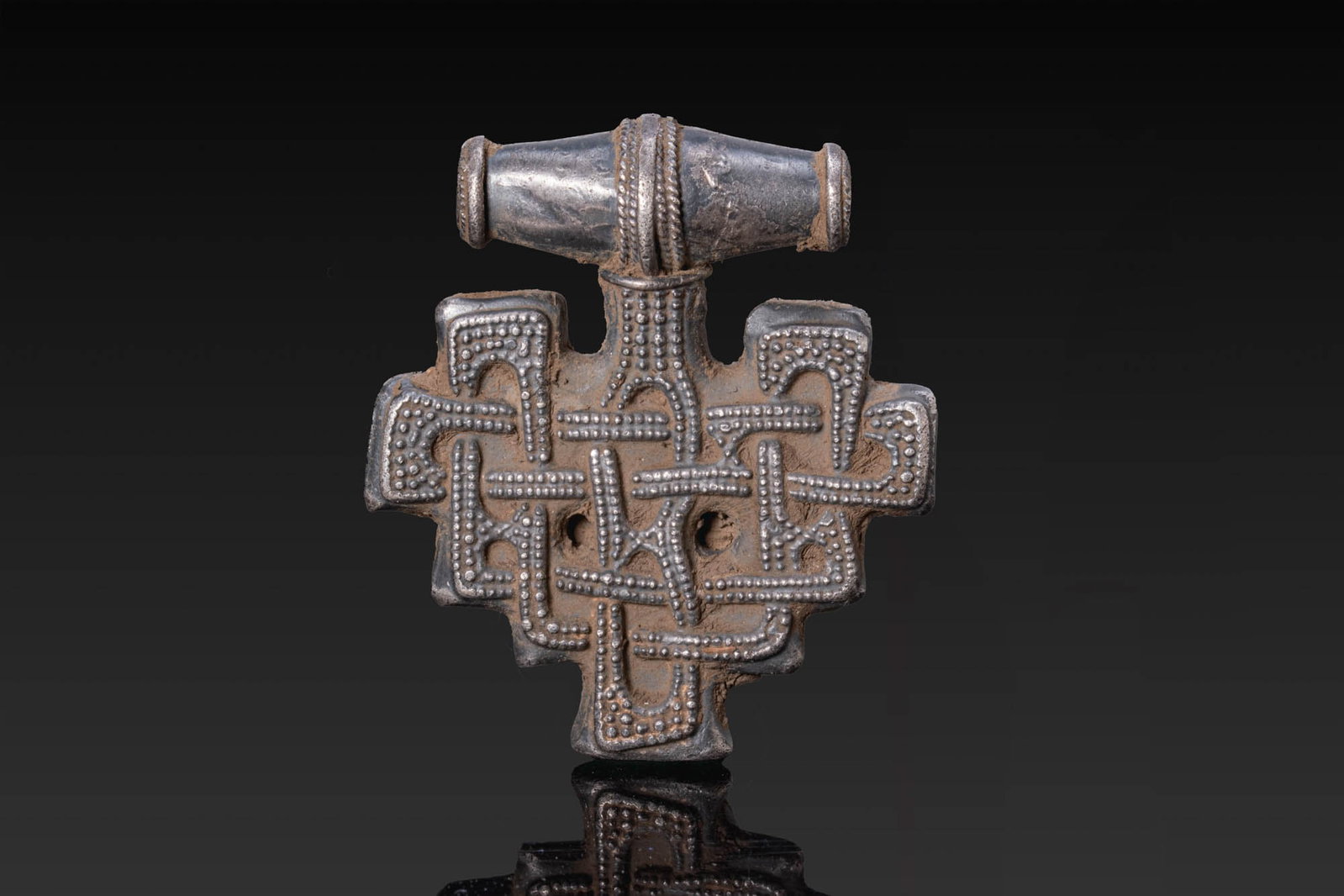 VIKING SILVER PENDANT WITH KNOT MOTIF: Ca. AD 900. A silver pendant of stepped cruciform outline. The obverse is decorated with interlacing bands bordered by rows of pellets, with two circular perforations at the centre. The loop is formed