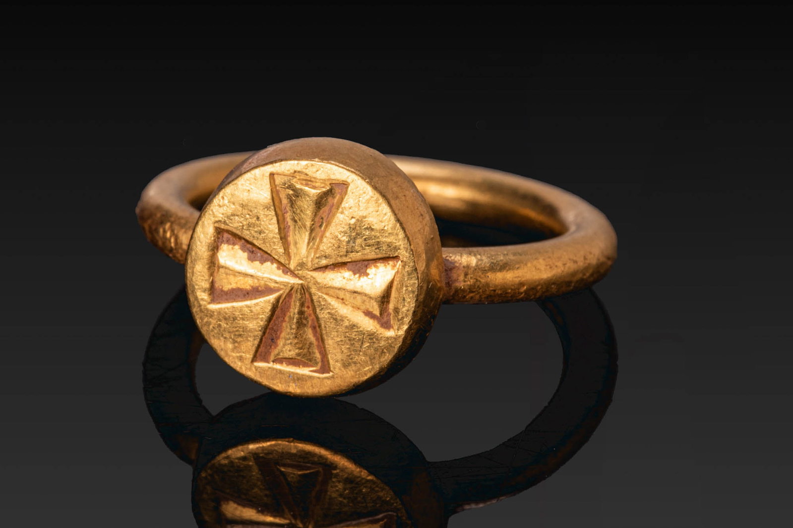 BYZANTINE GOLD RING WITH PATTEE CROSS: Ca. AD 600. A gold ring with a slender round-section hoop and an applied thick circular bezel engraved with a pattee cross formed of four recessed triangular arms. Size: D:12.4mm / US: 1 / UK: B; Weig