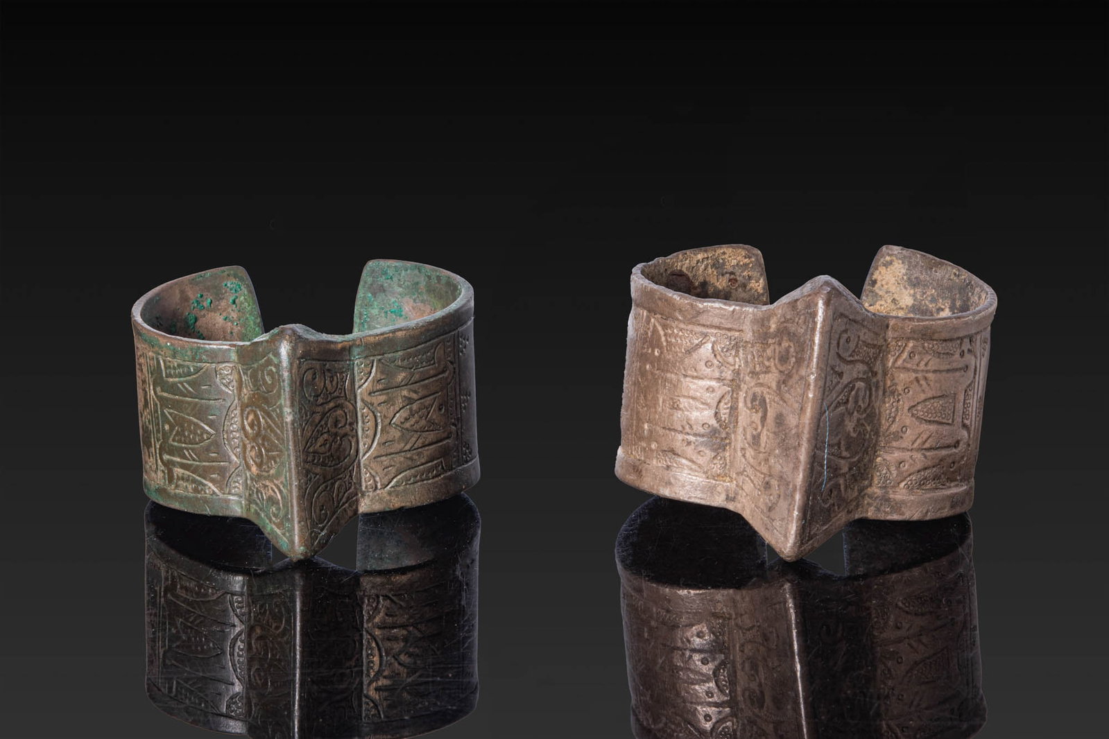 PAIR OF SELJUK SILVER BRACELETS: Ca. AD 1000 - 1100. A pair of silver bracelets, each of broad open form with a central ridge, slightly flaring terminals, and engraved panels of scrolling foliage and dotted ornament. Size: 58-60mm x 
