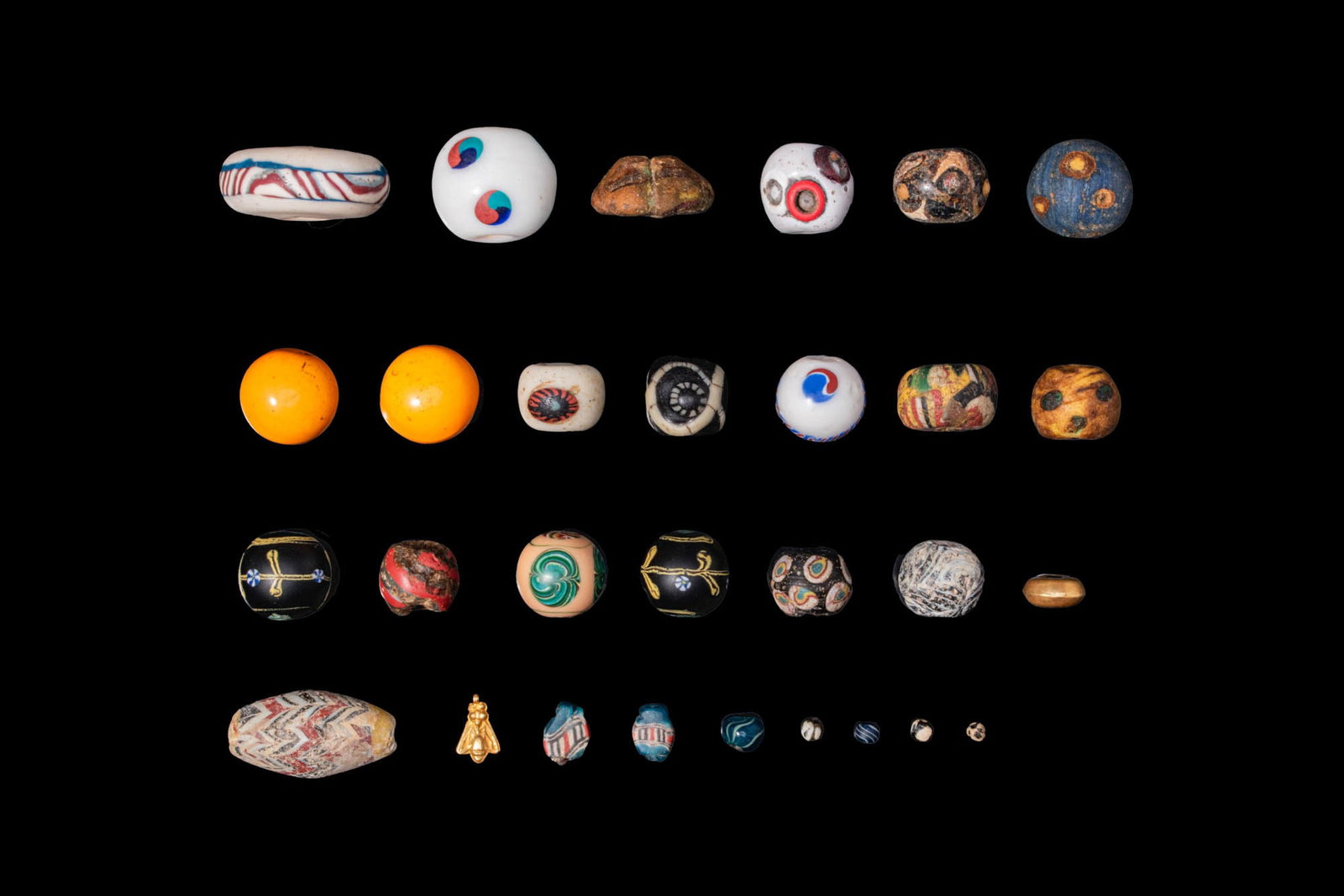 LARGE COLLECTION OF VENETIAN AND CHINESE GLASS BEADS: Ca. AD 1600 - 1800. A collection of 28 opaque and translucent glass beads, including spherical, biconical and flat examples, decorated with vivid polychrome canes, concentric eye motifs, and marbled a