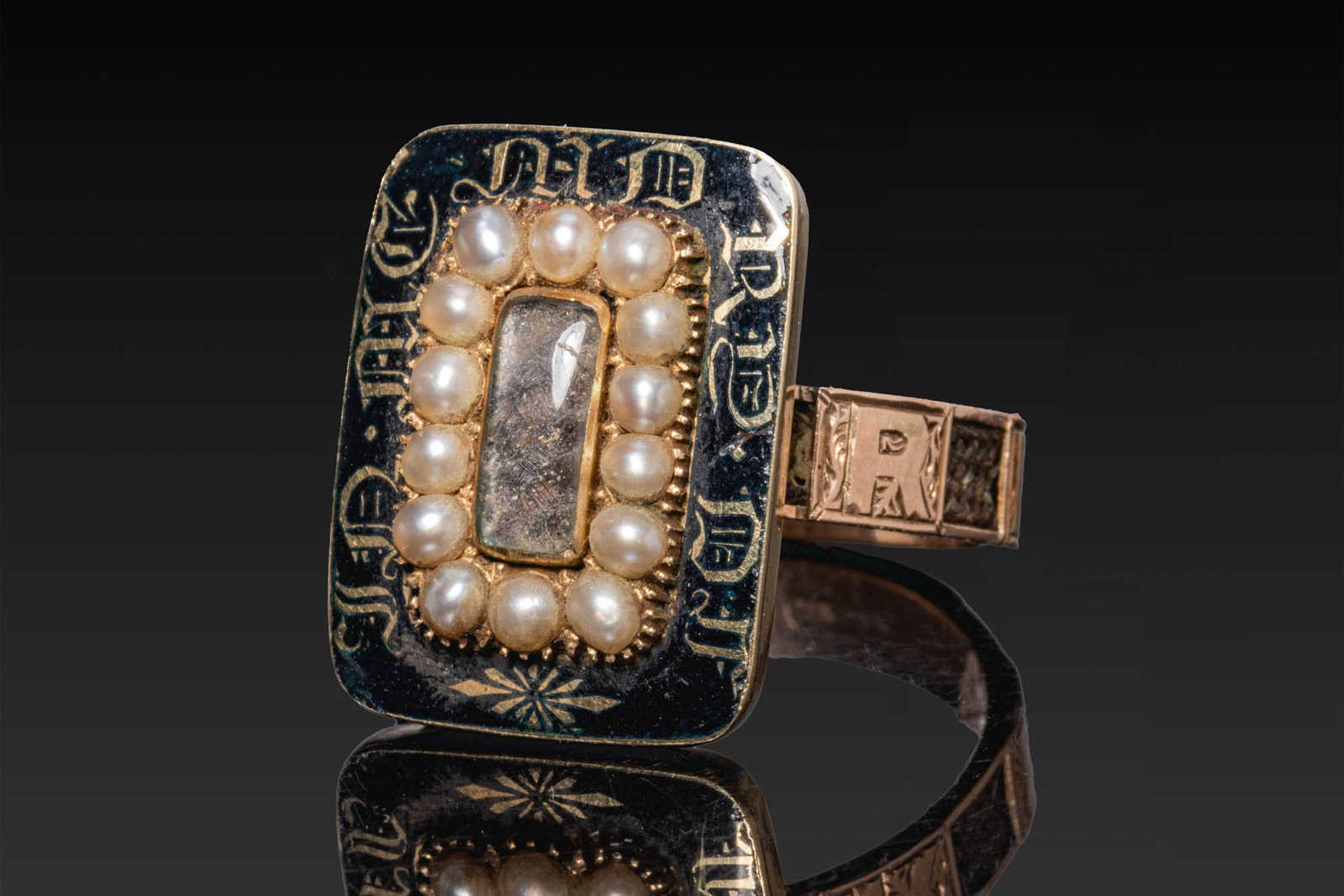 GEORGIAN GOLD MOURNING RING WITH HAIRWORK, PEARLS AND BLACK ENAMEL: Ca. AD 1826. A gold mourning ring with a large rectangular bezel centred on a rectangular glass panel within a border of pearls. The surrounding black enamel ground is inscribed in gilt 'IN MEMORY OF'