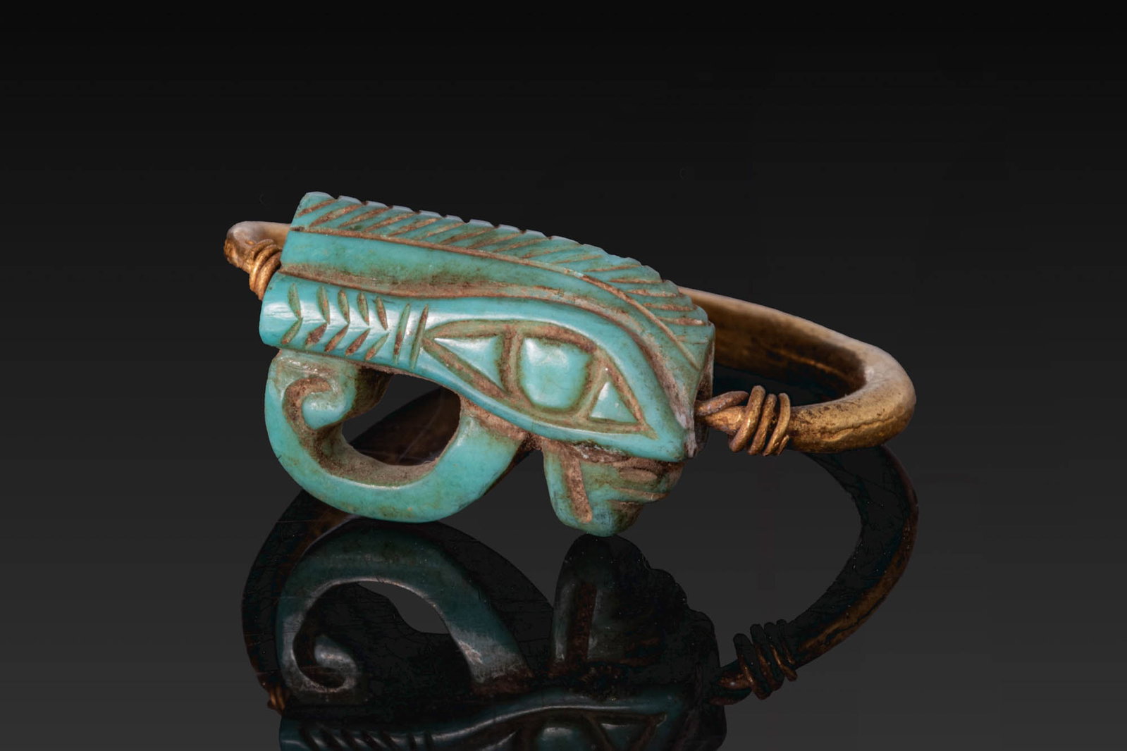EGYPTIAN SWIVEL GOLD RING WITH HORUS EYE AMULET: New Kingdom, Ca. 1550 - 1069 BC. A gold swivel ring with a rounded hoop and an openwork wedjat eye amulet mounted horizontally between wire collars. For similar see: The British Museum, Museum number 