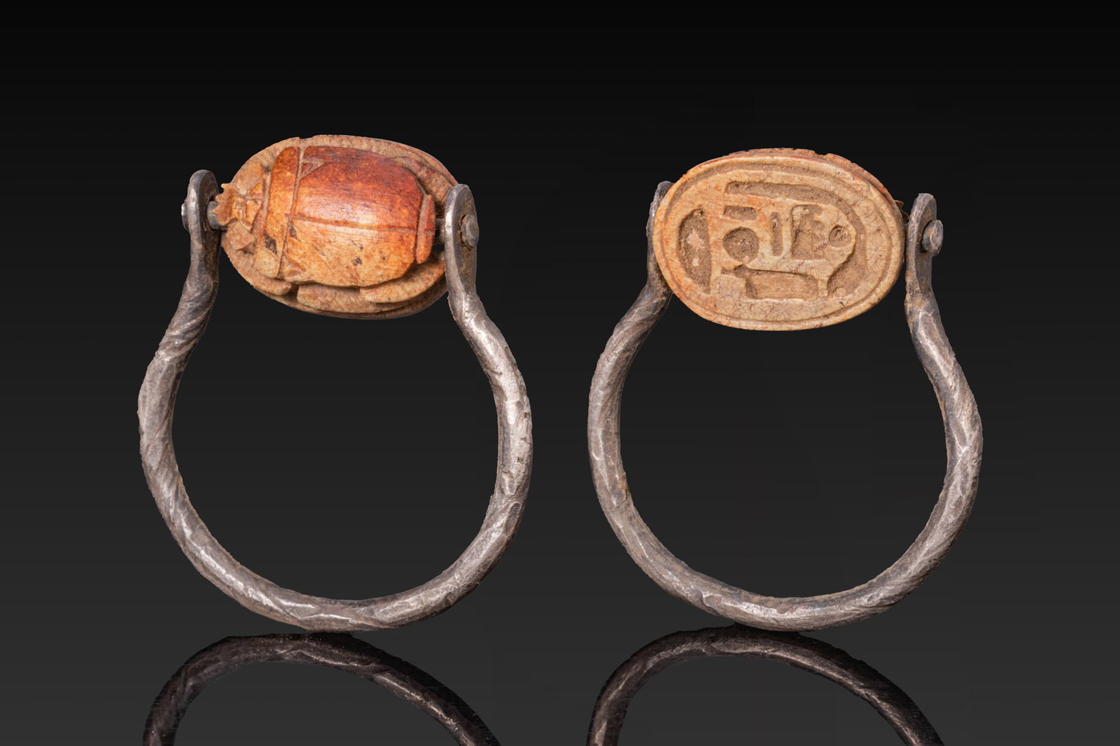 EGYPTIAN STEATITE SCARAB WITH THE NAME OF AMUN-RA IN SILVER SWIVEL RING: New Kingdom, Ca. 1550 - 1069 BC. A steatite scarab with a domed back marked by a single-line suture and pronotum separation, while V-shaped notches appear along the upper outer edges of the elytra. Th
