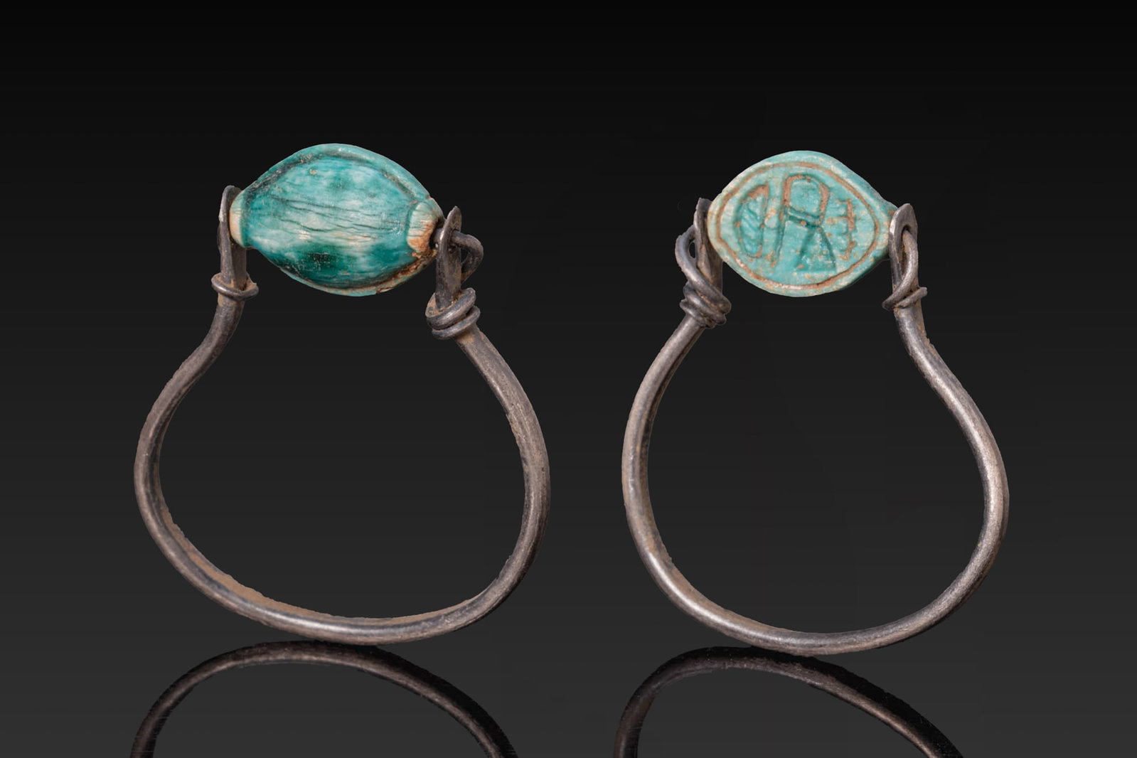 EGYPTIAN STEATITE COWROID WITH FLORAL COMPOSITION IN SILVER SWIVEL RING: Middle Kingdom to New Kingdom, Ca. 2030 - 1069 BC. A blue-glazed steatite cowroid, a seal-amulet derived from the shape of the cowrie shell (used in Egypt from early times as both an ornament and a sy