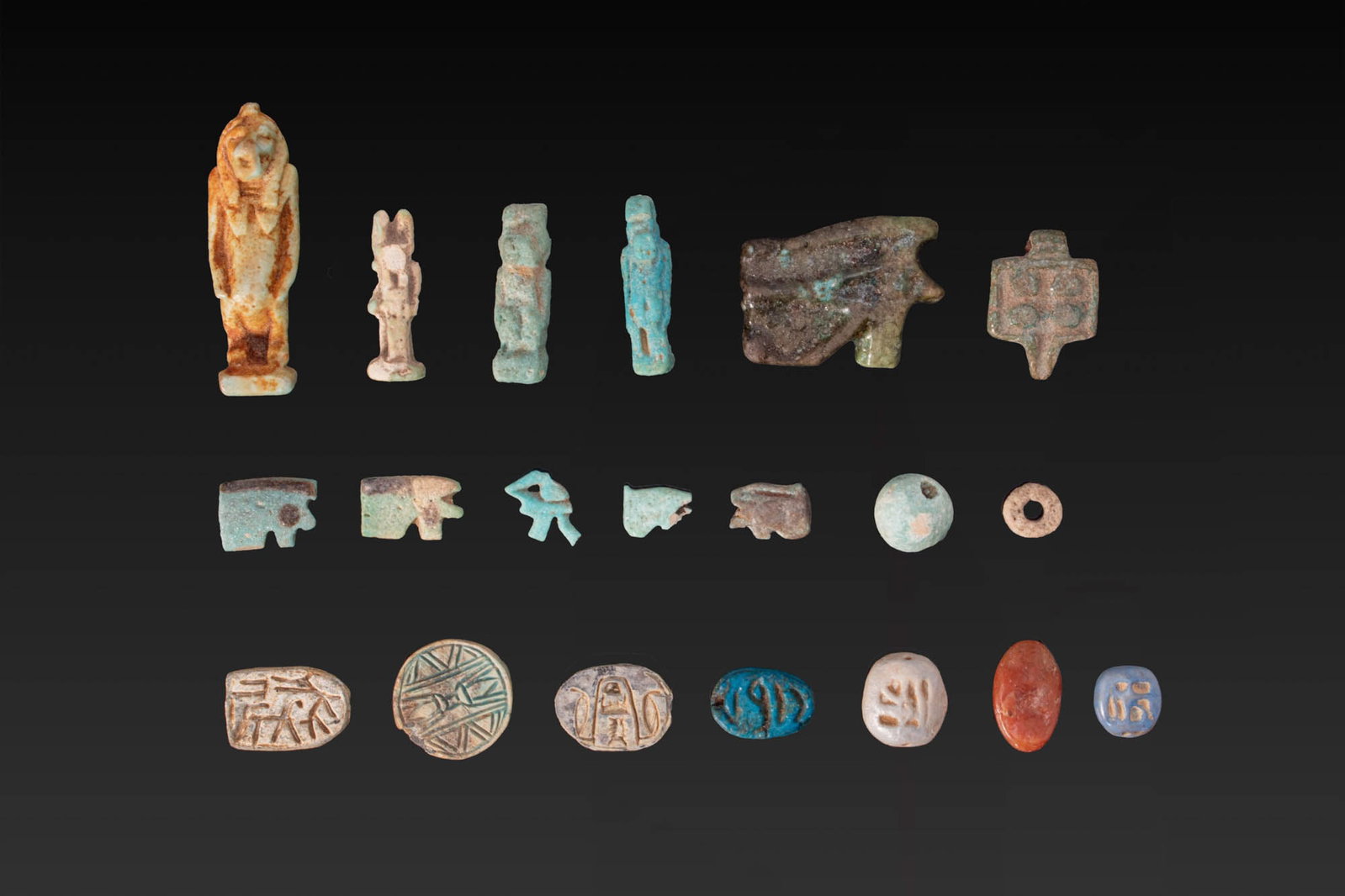 LARGE COLLECTION OF EGYPTIAN FAIENCE AND STONE AMULETS: New Kingdom to Ptolemaic Period, Ca. 1550 - 30 BC. A collection of 20 faience and stone amulets, beads, scarabs, and scaraboids, including, from left to right: a standing Taweret; a standing Anubis wi