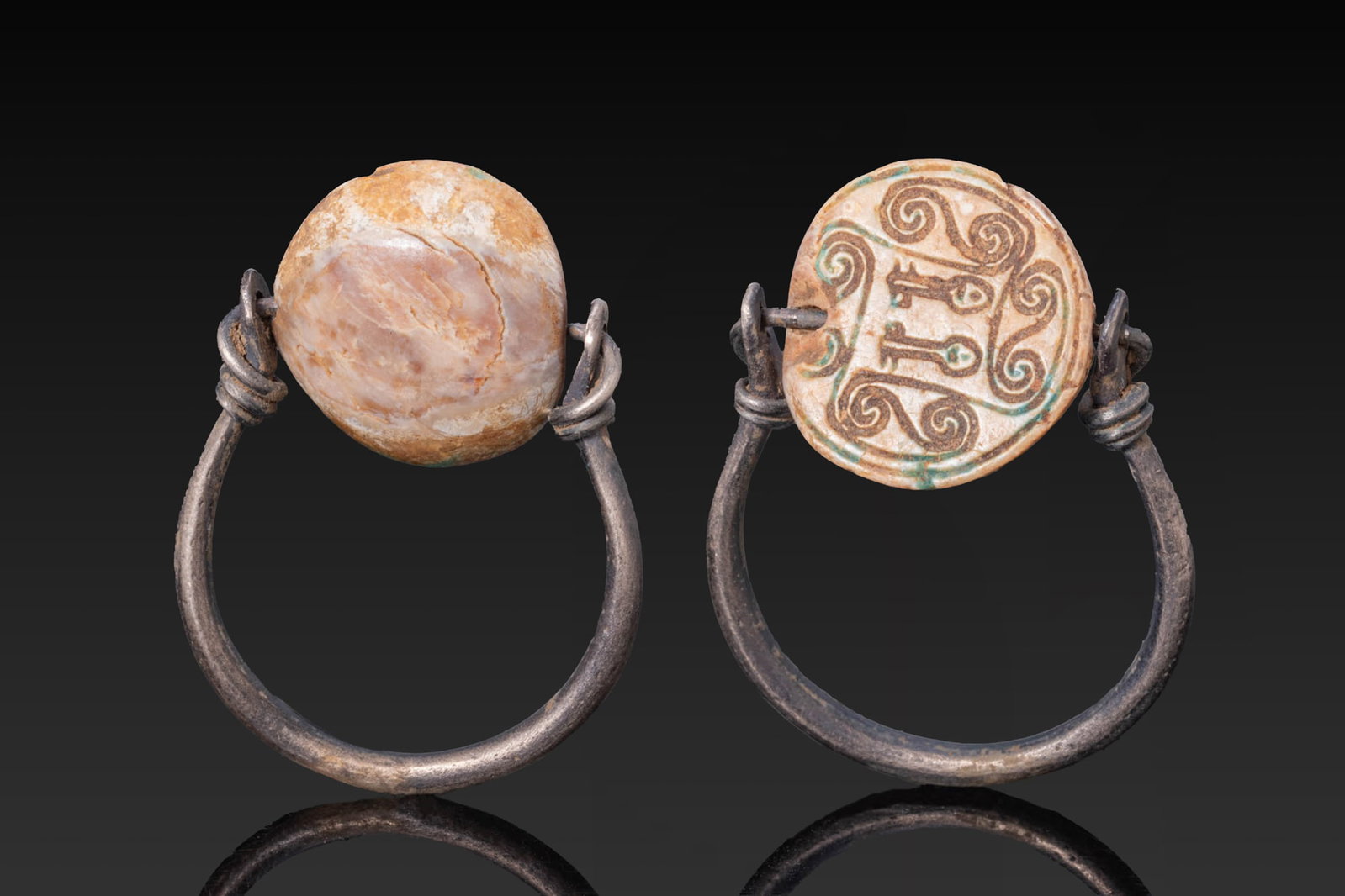 EGYPTIAN STEATITE ROUNDED SCARABOID WITH NEFER SIGNS AND SCROLLS IN SILVER SWIVEL RING: Middle Kingdom, Ca. 2030 - 1640 BC. A steatite rounded-shaped scaraboid (button seal?) preserving traces of blue glaze, with no detail, and set in a possibly later silver swivel ring with a plain hoop