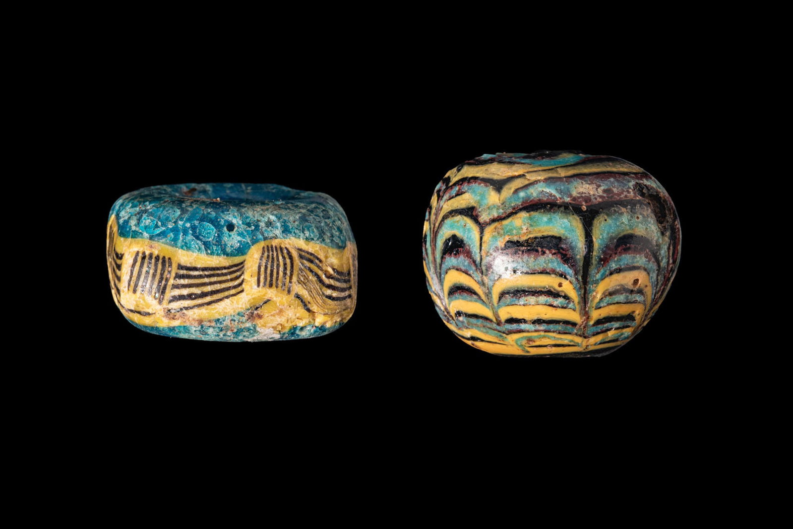 PAIR OF PHOENICIAN GLASS BEADS: Ca. 600 - 400 BC. A pair of glass beads, from left to right: a turquoise glass bead of compressed cylindrical form, decorated at the midsection with a broad yellow band overlaid with closely set dark 