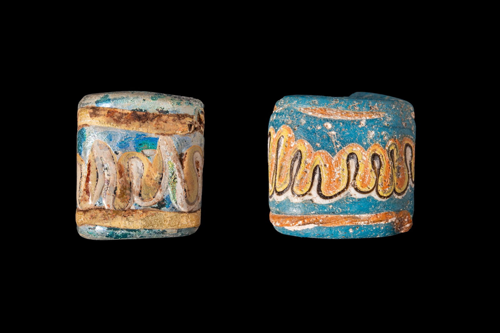 PAIR OF PHOENICIAN GLASS BEADS WITH WAVE MOTIFS: Ca. 600 - 400 BC. A pair of turquoise glass beads of rectangular section, from left to right: a bead decorated with an undulating white and yellow wave motif between yellow horizontal bands; and a bea