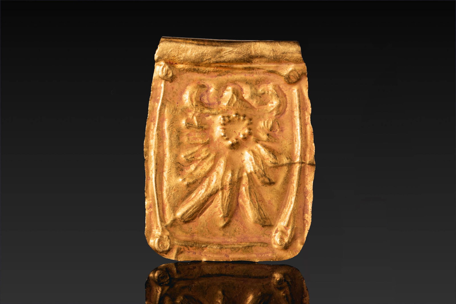 GREEK GOLD PLAQUE WITH MYTHOLOGICAL SUBJECT: Ca. 800 - 600 BC. A rectangular gold plaque with a rolled upper edge and rounded lower corners. The field is decorated in repousse with a mythological figure within a narrow border, with bosses at the